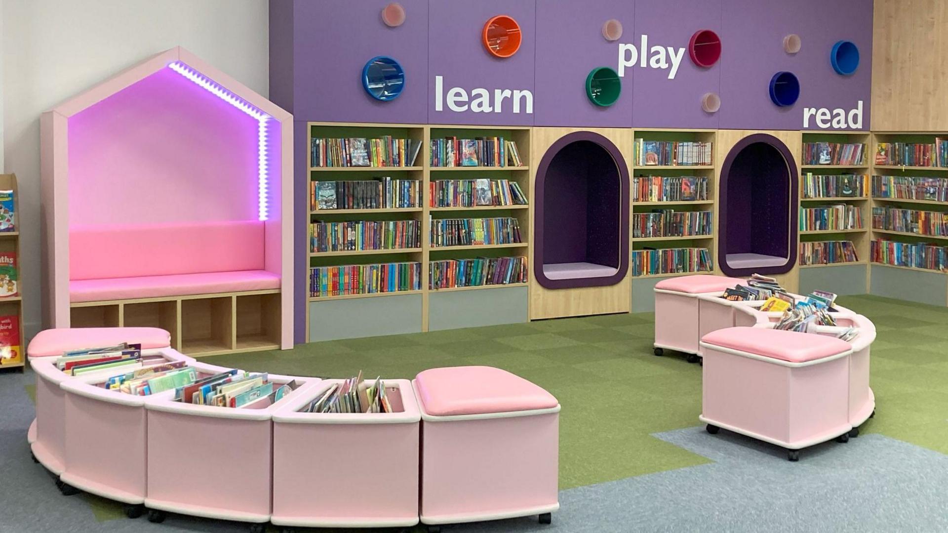 A  section of library with pink book storage and benches, as well as purple sitting nooks. 