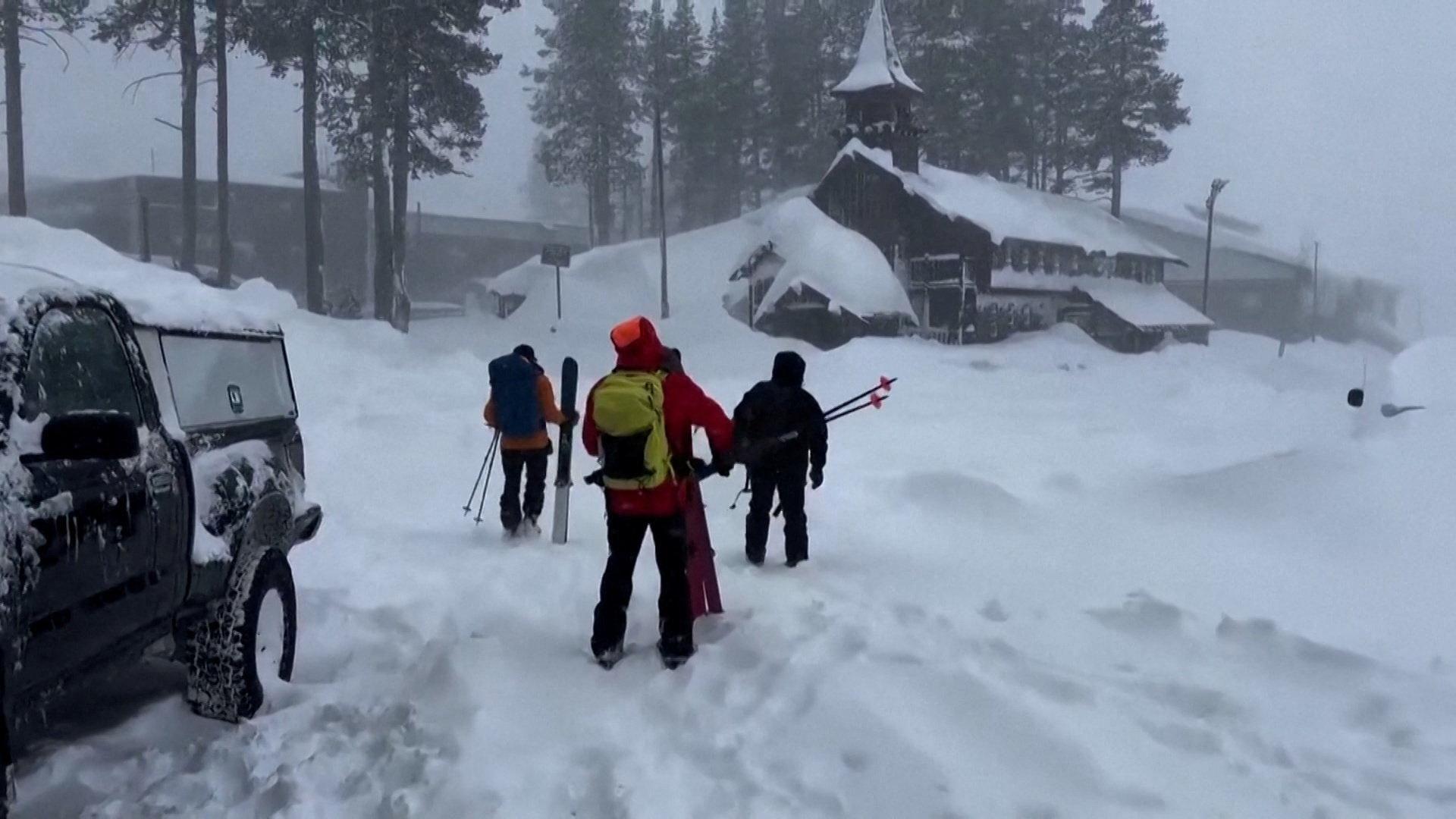 A ski rescue team of three departs for the site of Tuesday's deadly avalanche in Nevada County, California on 17 February, through thick snow, with an SUV in the foreground and a church heavily laden with snow ahead of them.