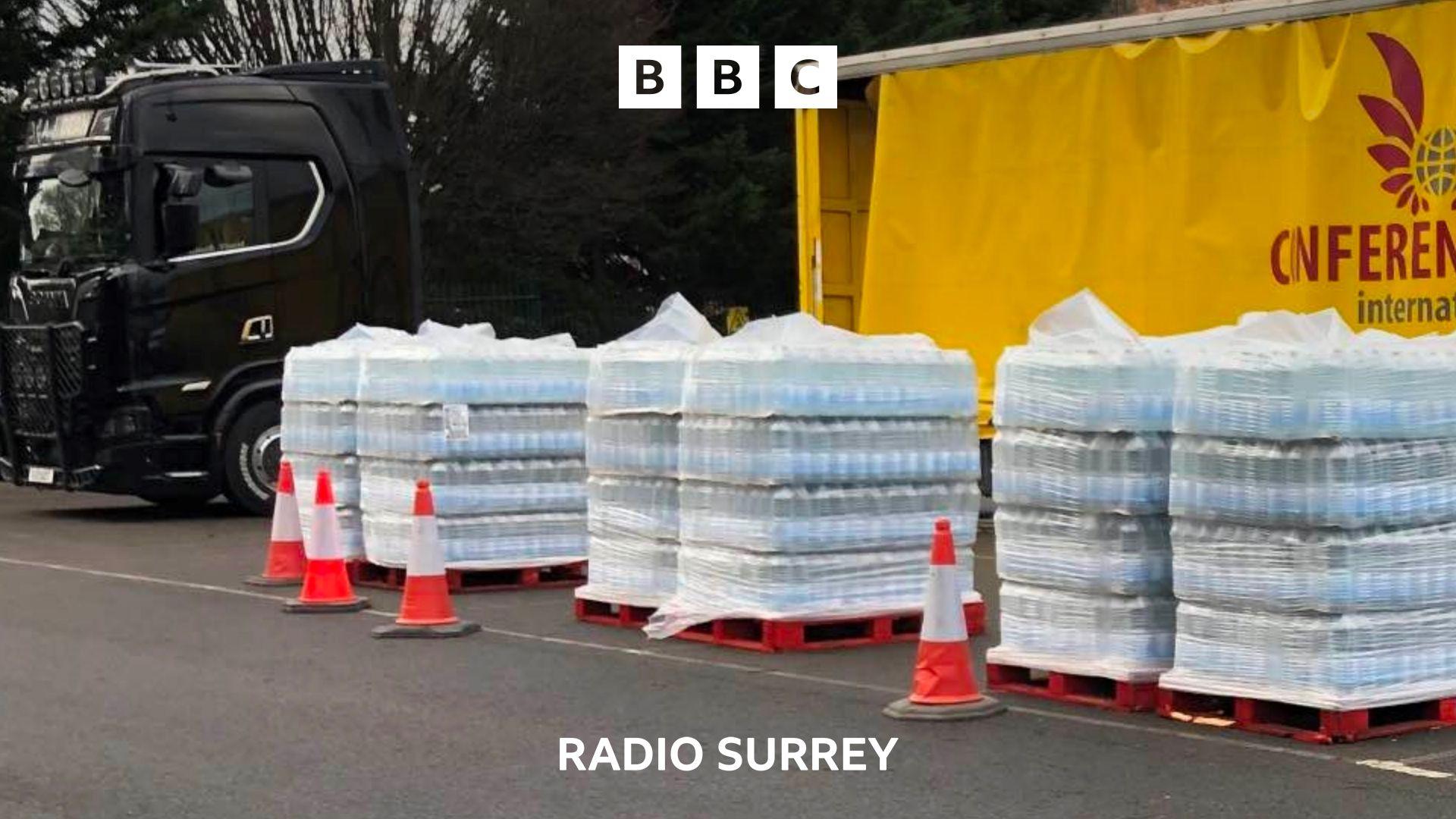 Crates of bottled water are lined up in front of a yellow lorry.