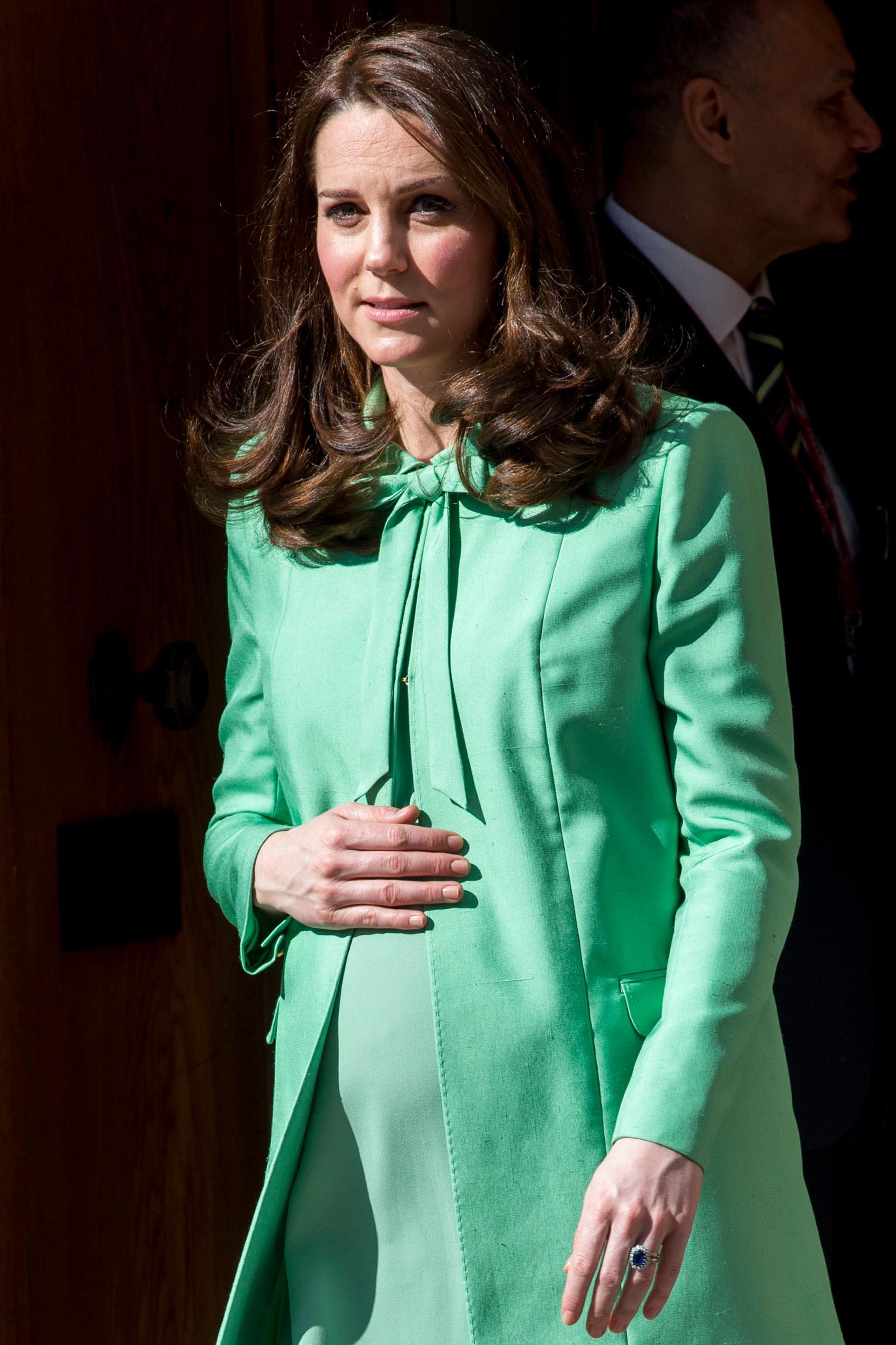 A photo of Catherine Middleton wearing Green during her pregnancy, she's holding a visible bump and grimacing 