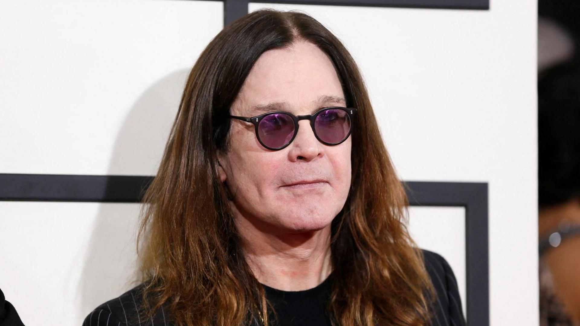 Ozzy Osbourne, wearing black-rimmed glasses with dark lenses, looks just off camera.