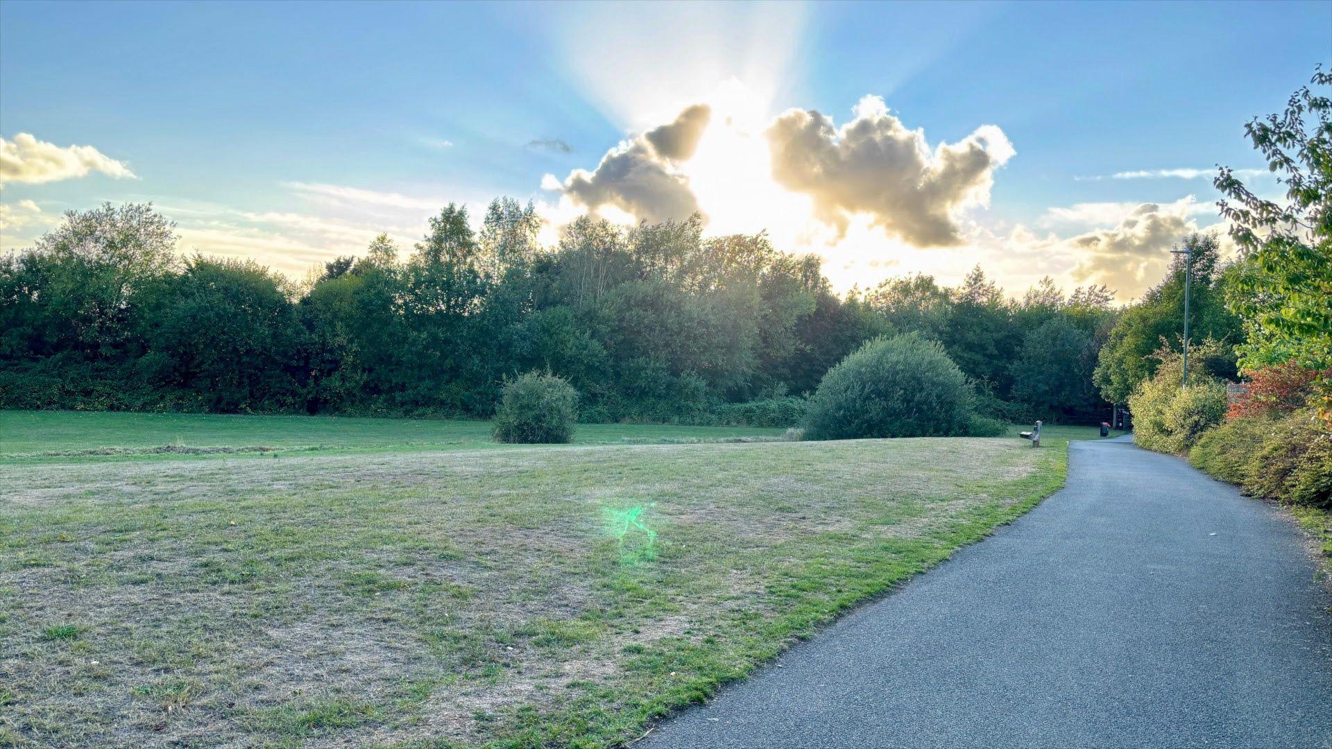 Sun breaking through the clouds on a pathway with green grass next to it.
