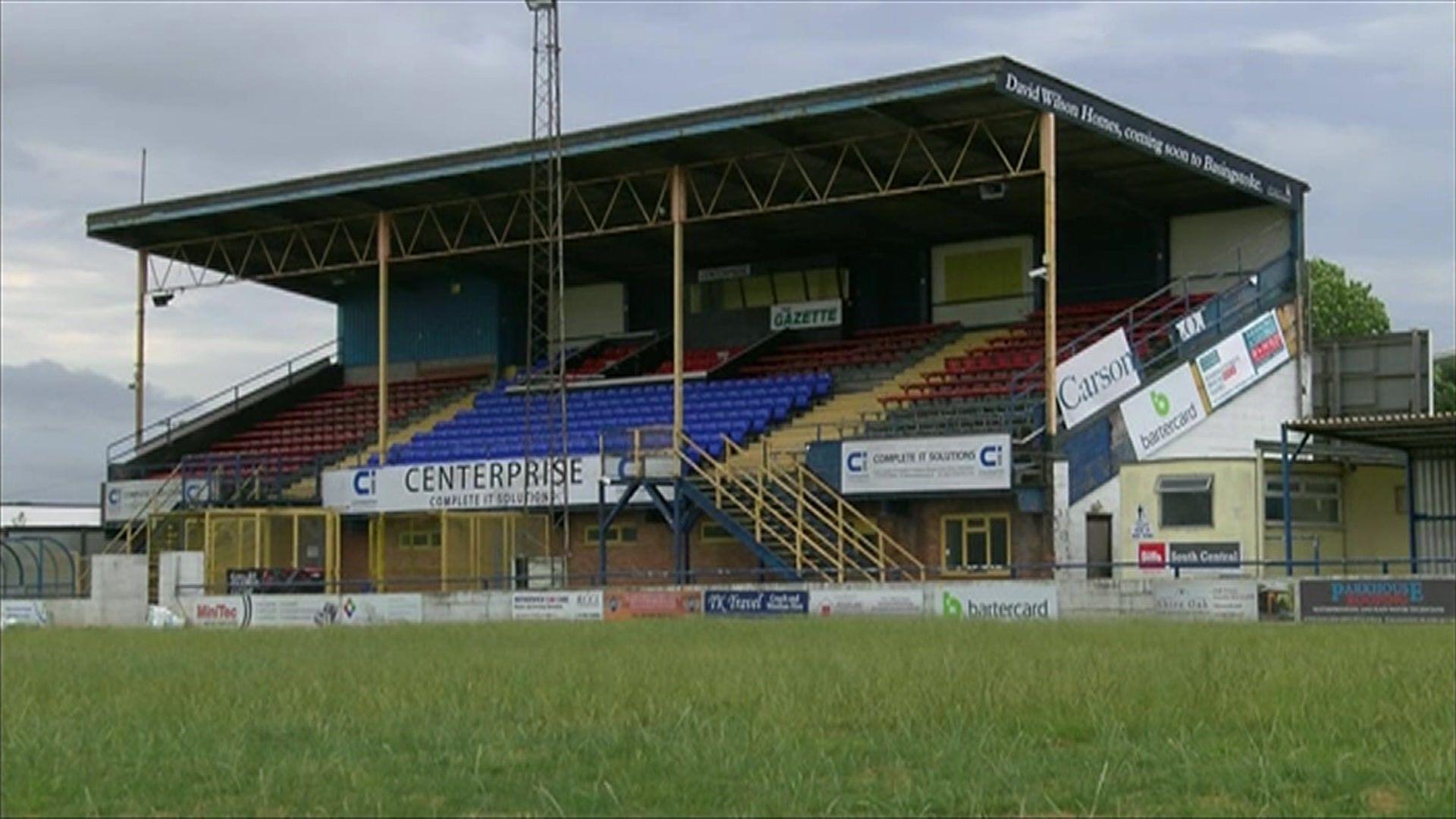 A large grandstand with red and blue seats looking out on to a grass pitch.