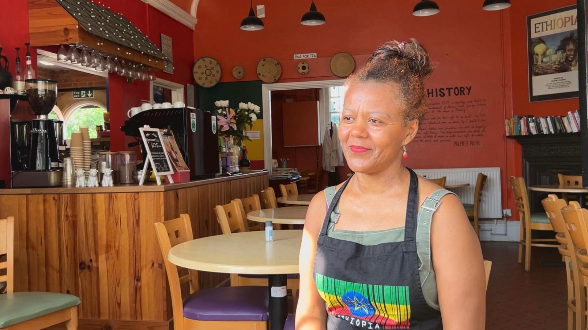 An image of Tutu Melaku sat in her cafe with an apron on