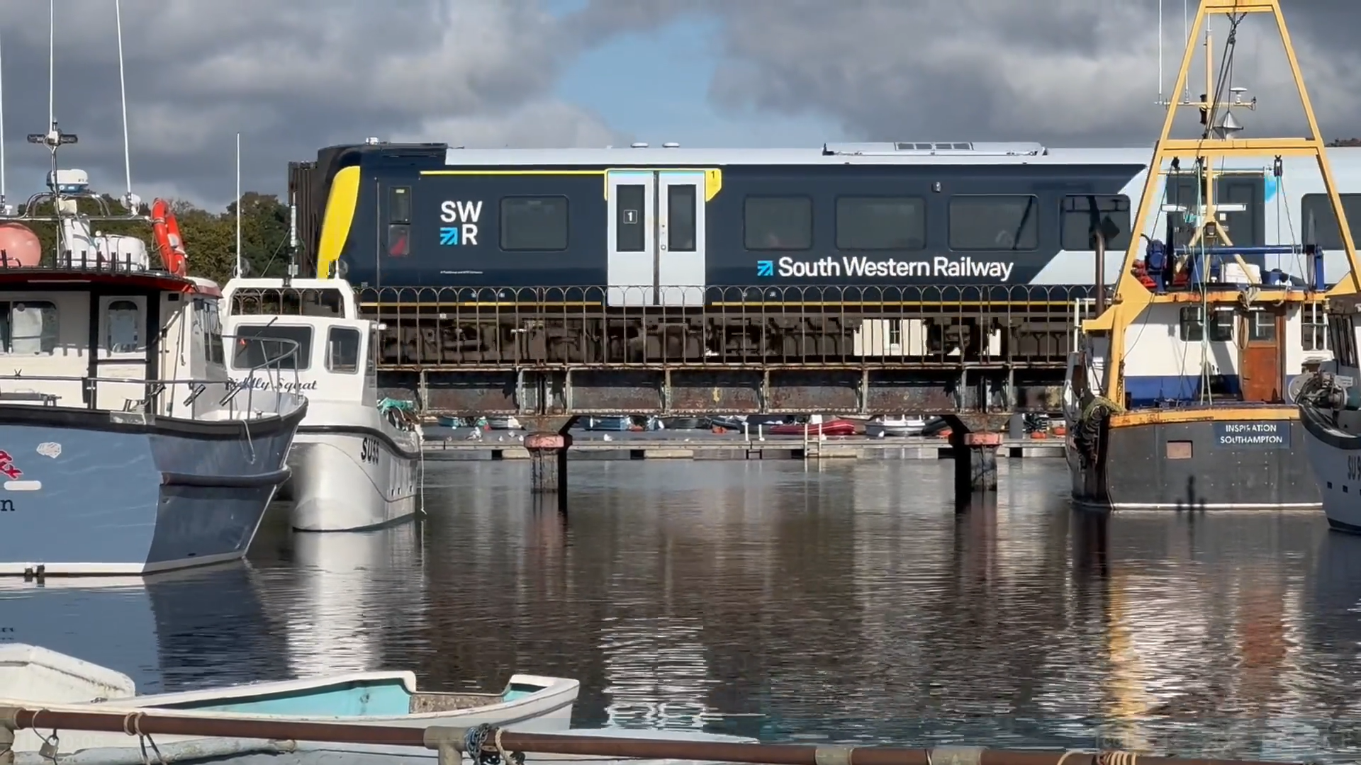 A train crosses a viaduct over Lymington River, which has several moored boats.