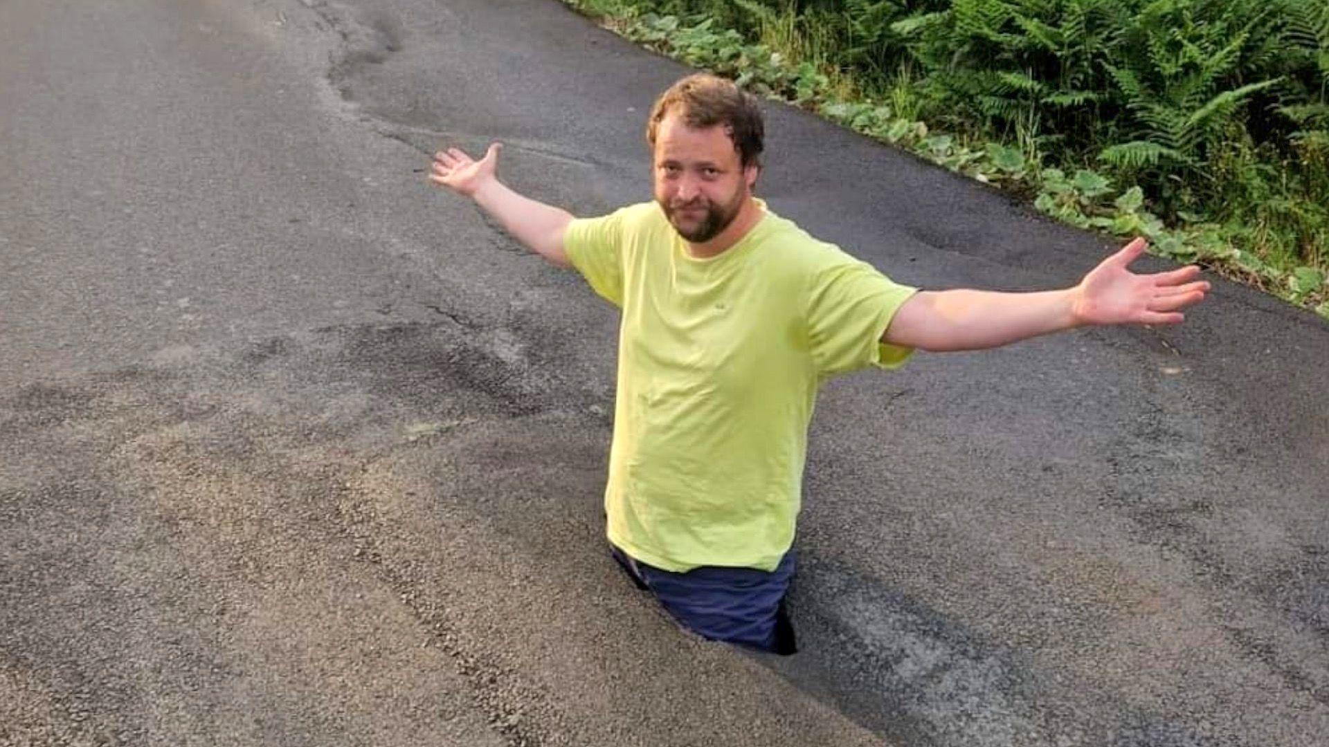 Malachy Quinn standing almost up to his waist in a deep pothole - he's wearing a yellow t-shirt and blue jeans, and standing with his arms outstretched 