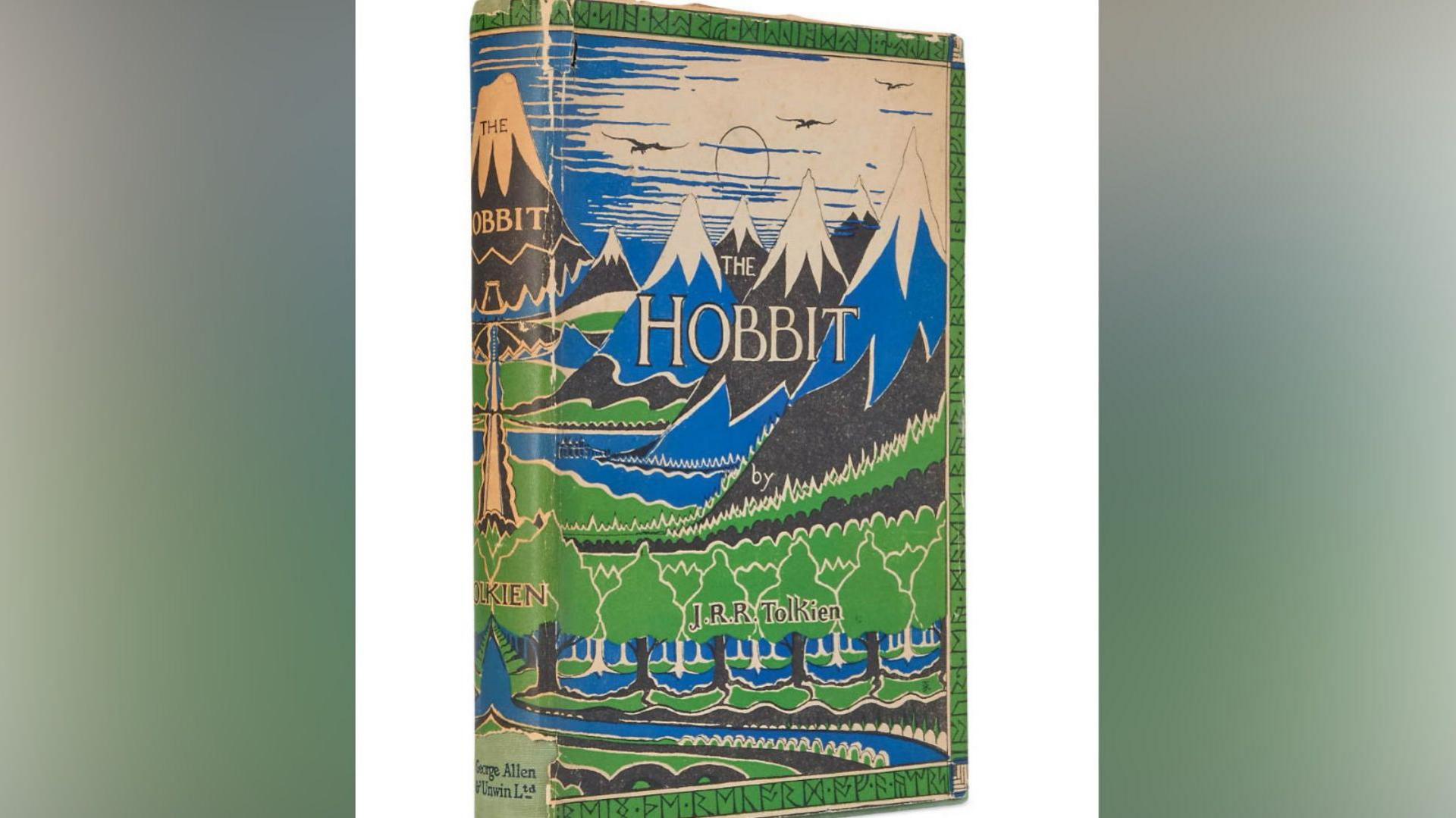 Worn vintage hardback copy of 'The Hobbit' by J.R.R. Tolkien, showing the original illustrated dust jacket with blue and green mountain, forest and river artwork, photographed against a plain background