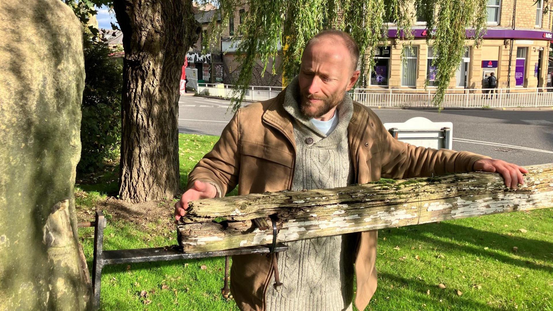 A man tends to a large wooden gate which appears rotten. The wood is attached to a metal black post