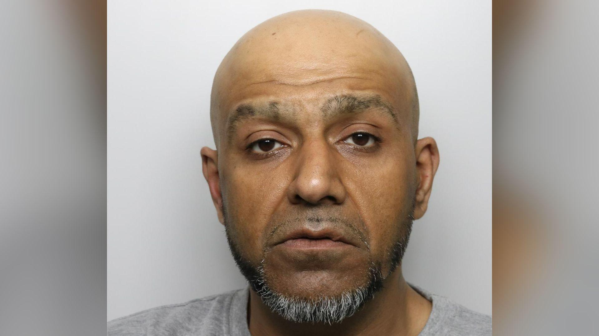 A mugshot of Saqib Khan, with a bald head and a goatee beard.