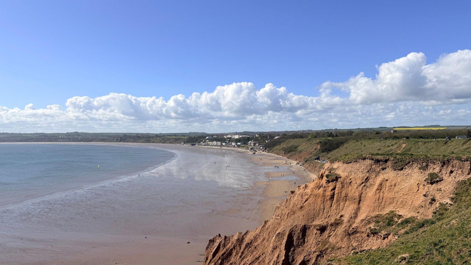 A landscape photo of the sea and some cliffs, with blue sky and cumulus clouds overhead