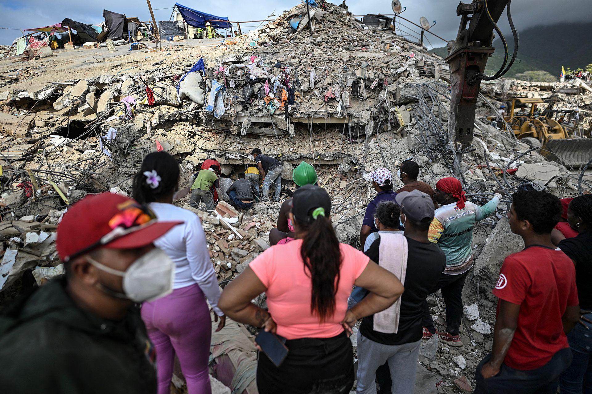A group of people stand with their backs to the camera while search teams navigate the rubble of a destroyed building, in Caraballeda, Venezuela on 22 July.