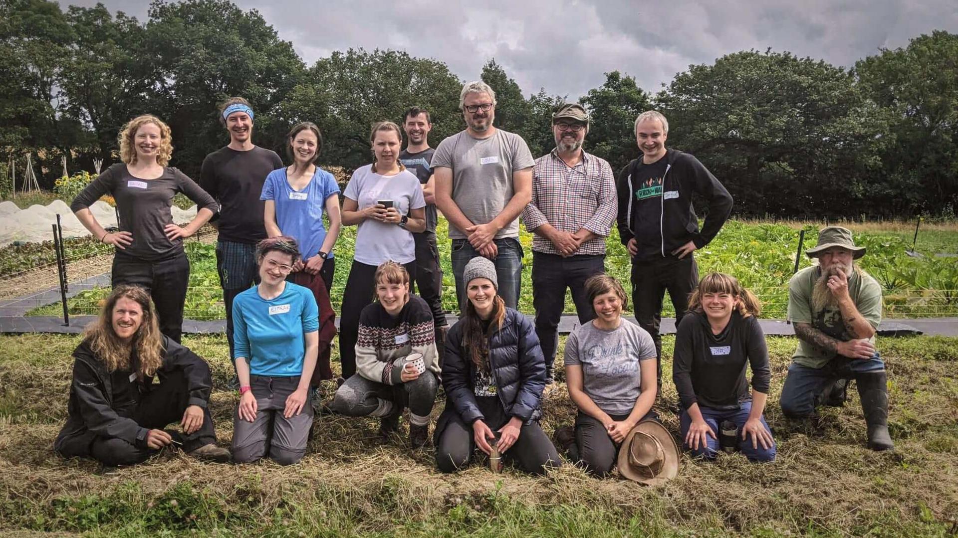 A large group of people dressed in casual clothing pose for a photo in two rows on farmland