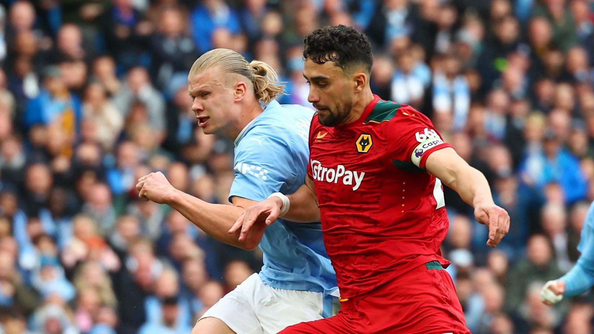 Max Kilman, wearing Wolves' red away kit, challenges Manchester City's Erling Haaland on his left side as they both run for the ball