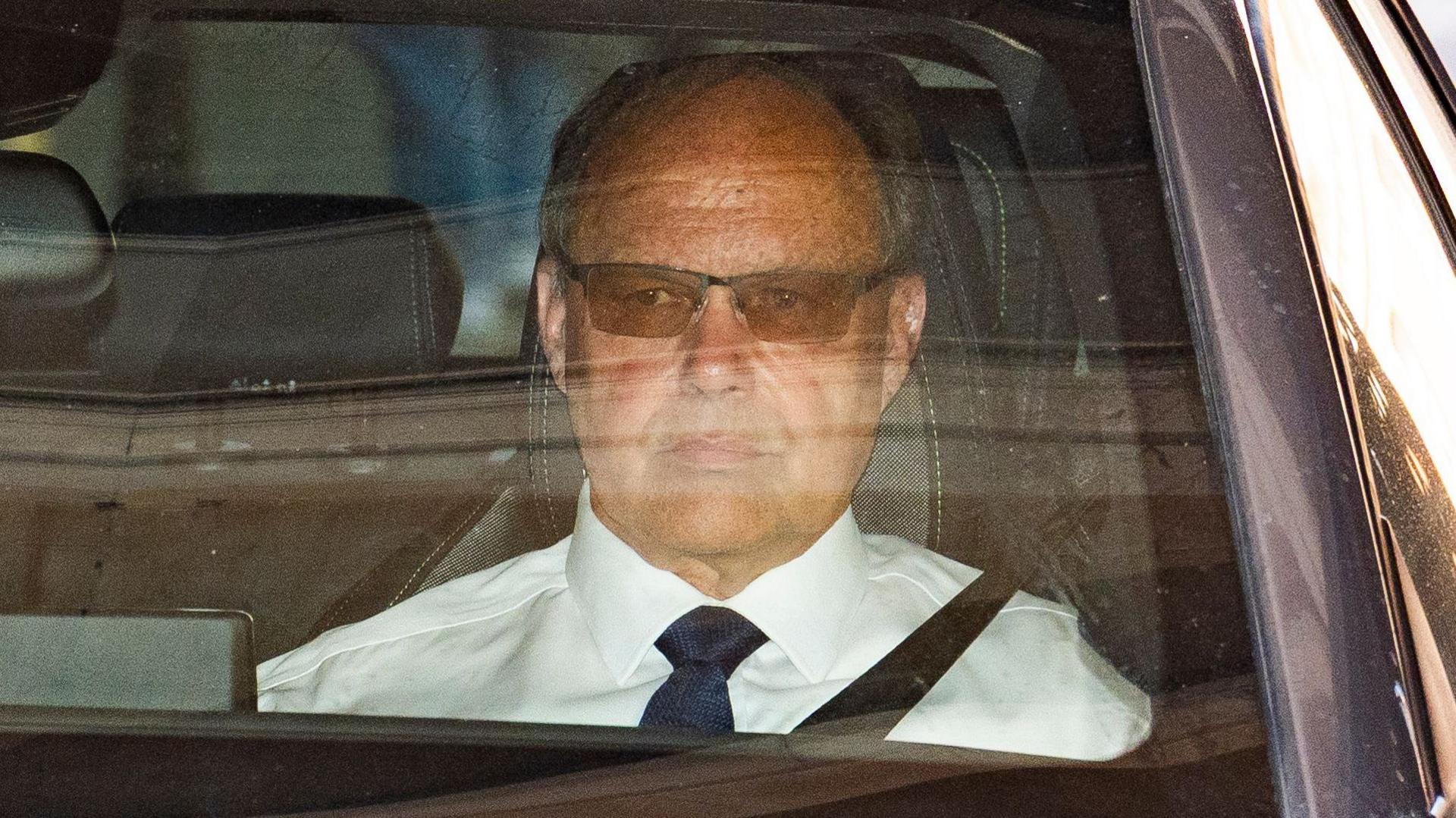 Glyn Razzell leaving the High Court hearing the passenger seat of a car. He is wearing a white shirt, black tie and tinted glasses.