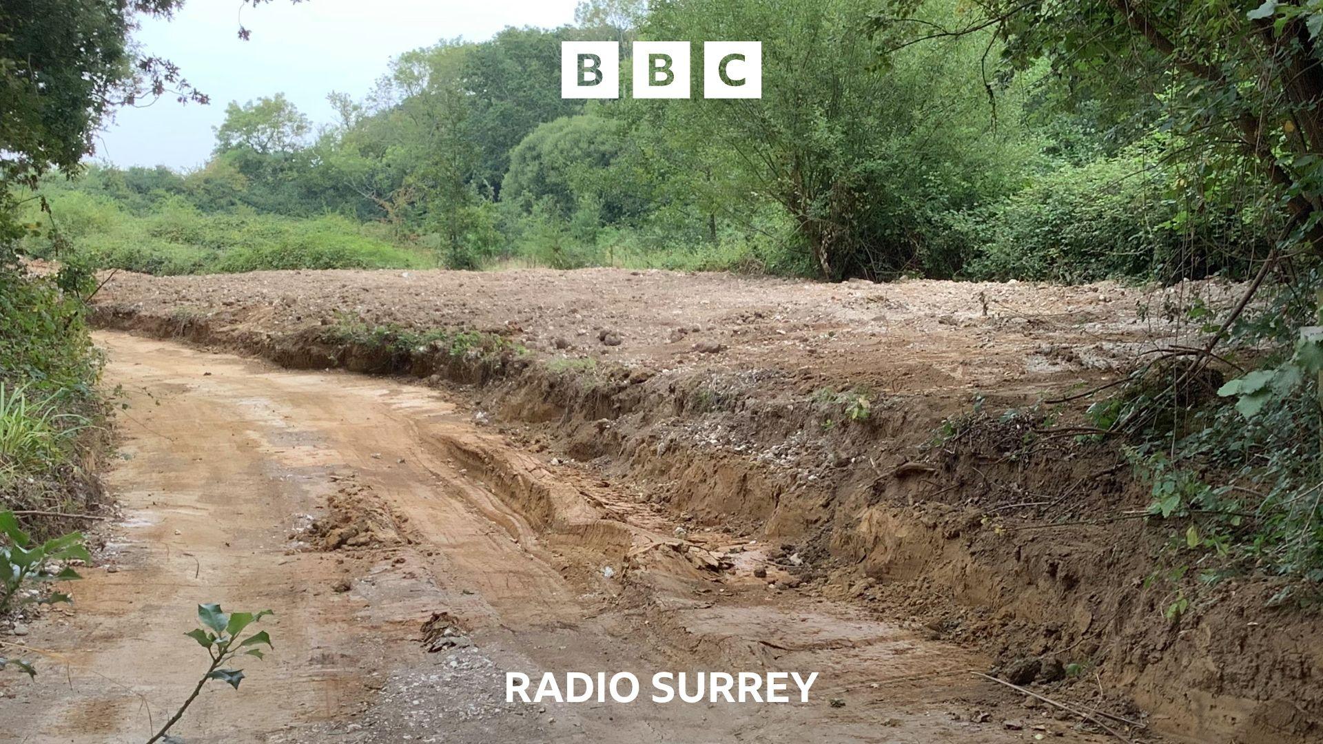 A freshly dug, muddy track leads off around a tree lined corner.