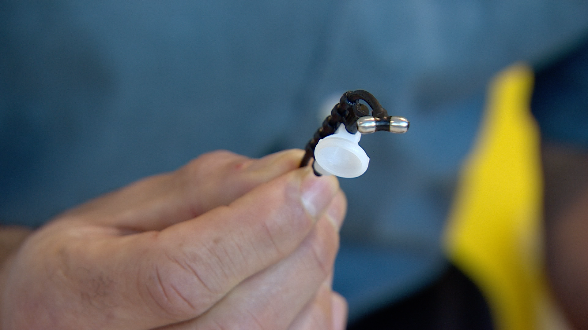 A man's hand holds up a small device which looks like a hearing aid