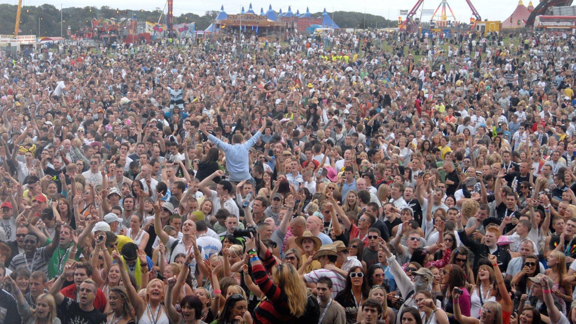 Hundreds of people can be seen in a concert crowd with arms aloft.