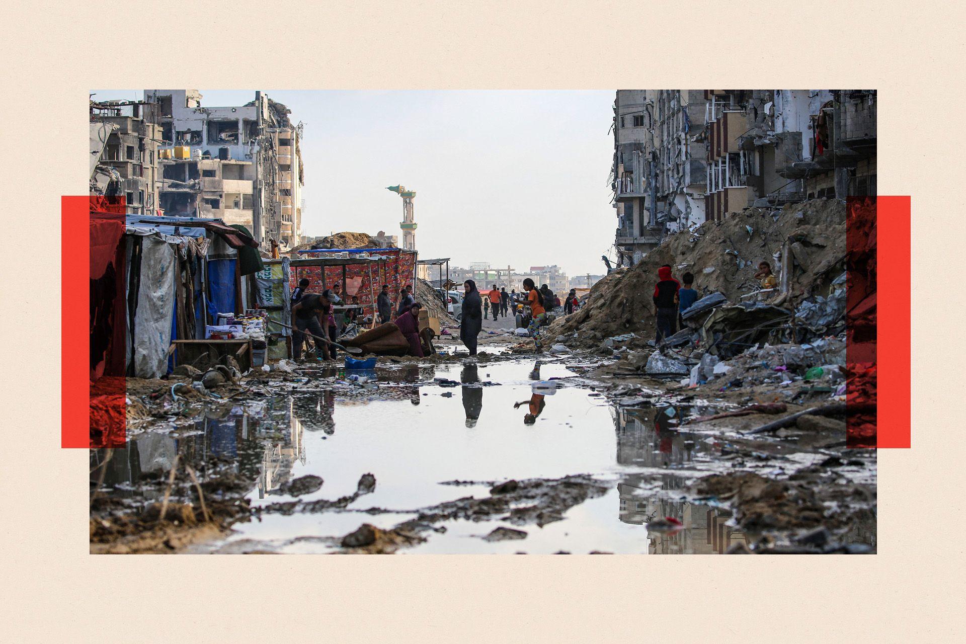 Displaced Palestinians walk around a puddle in front of destroyed buildings and tents in Khan Yunis in the southern Gaza Strip in May 2024