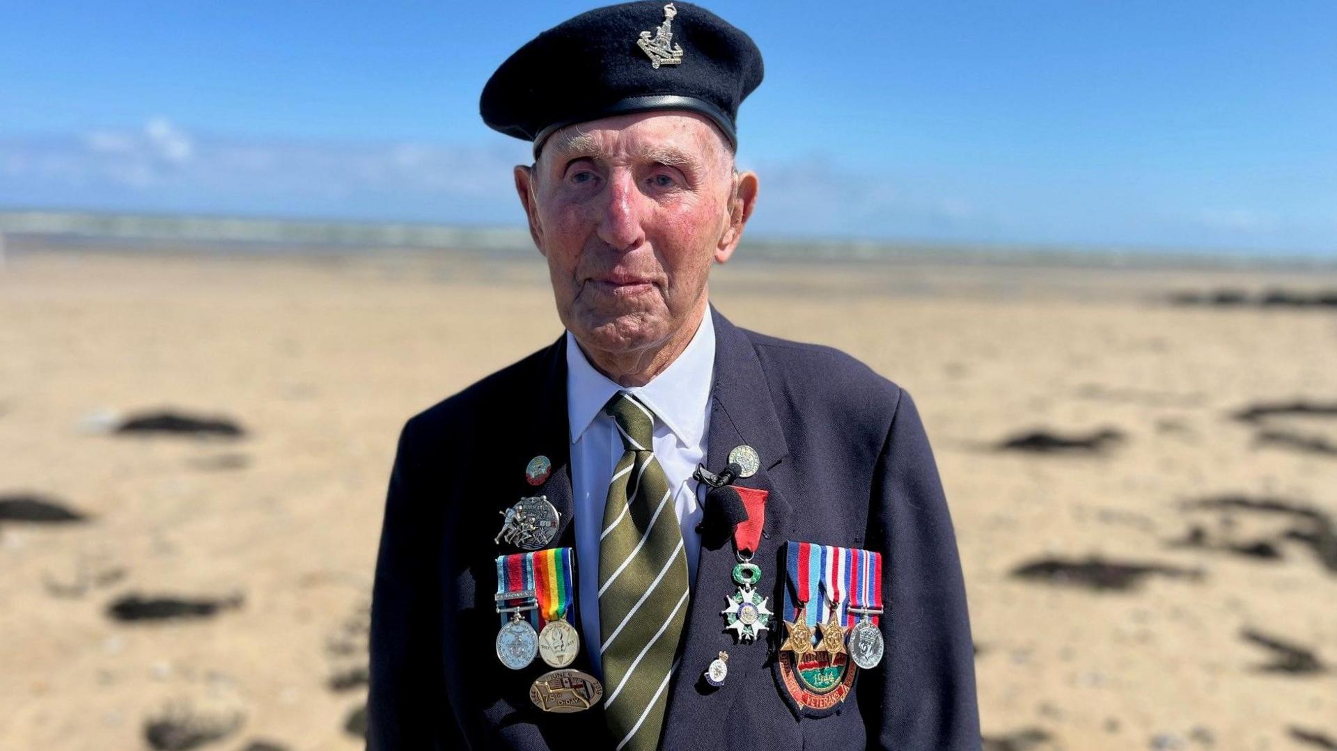 An old man wears a beret with insignia and a jackt festooned with medals