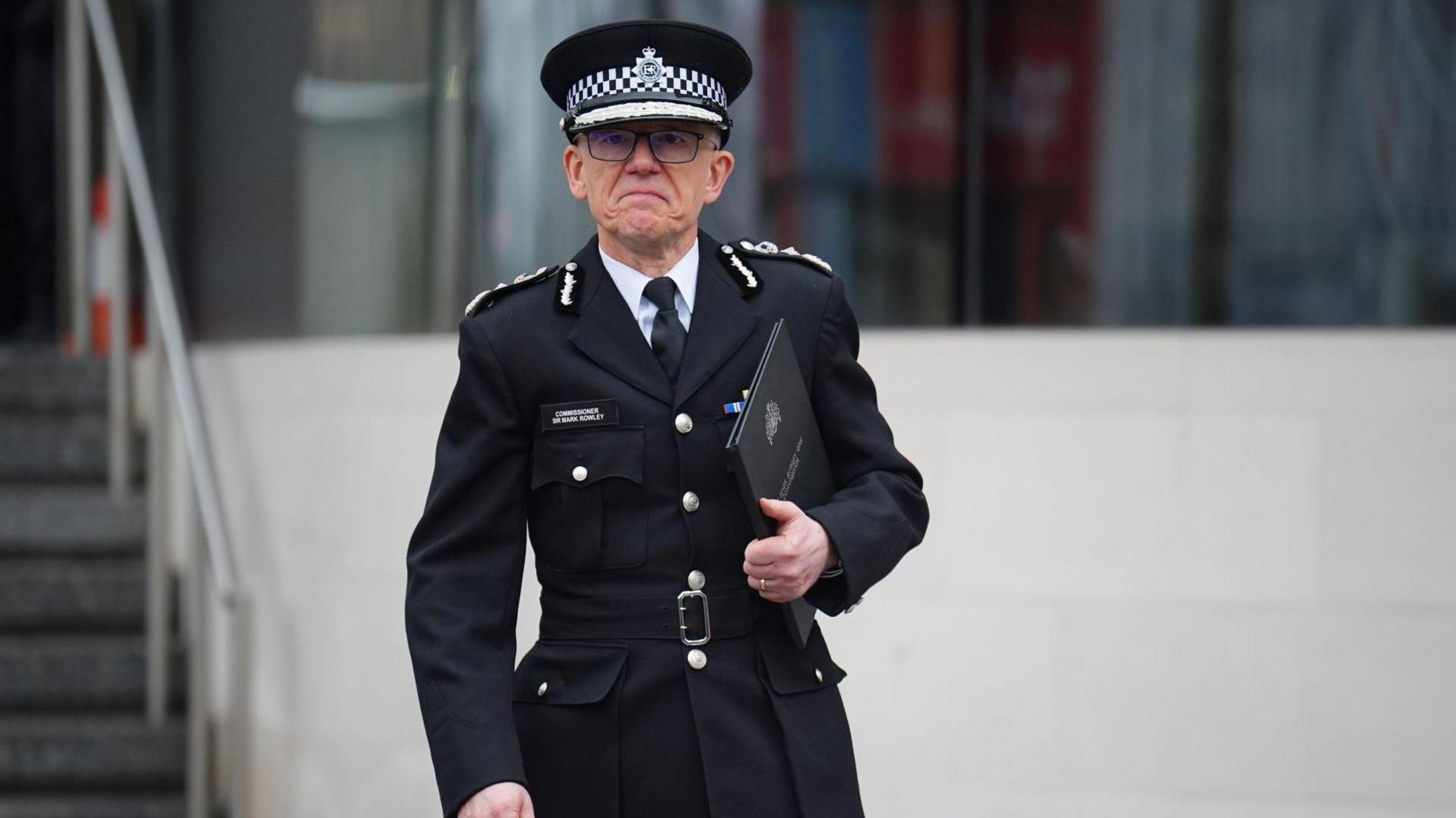 Sir Mark Rowley, in police uniform, holding a folder on the steps of New Scotland Yard