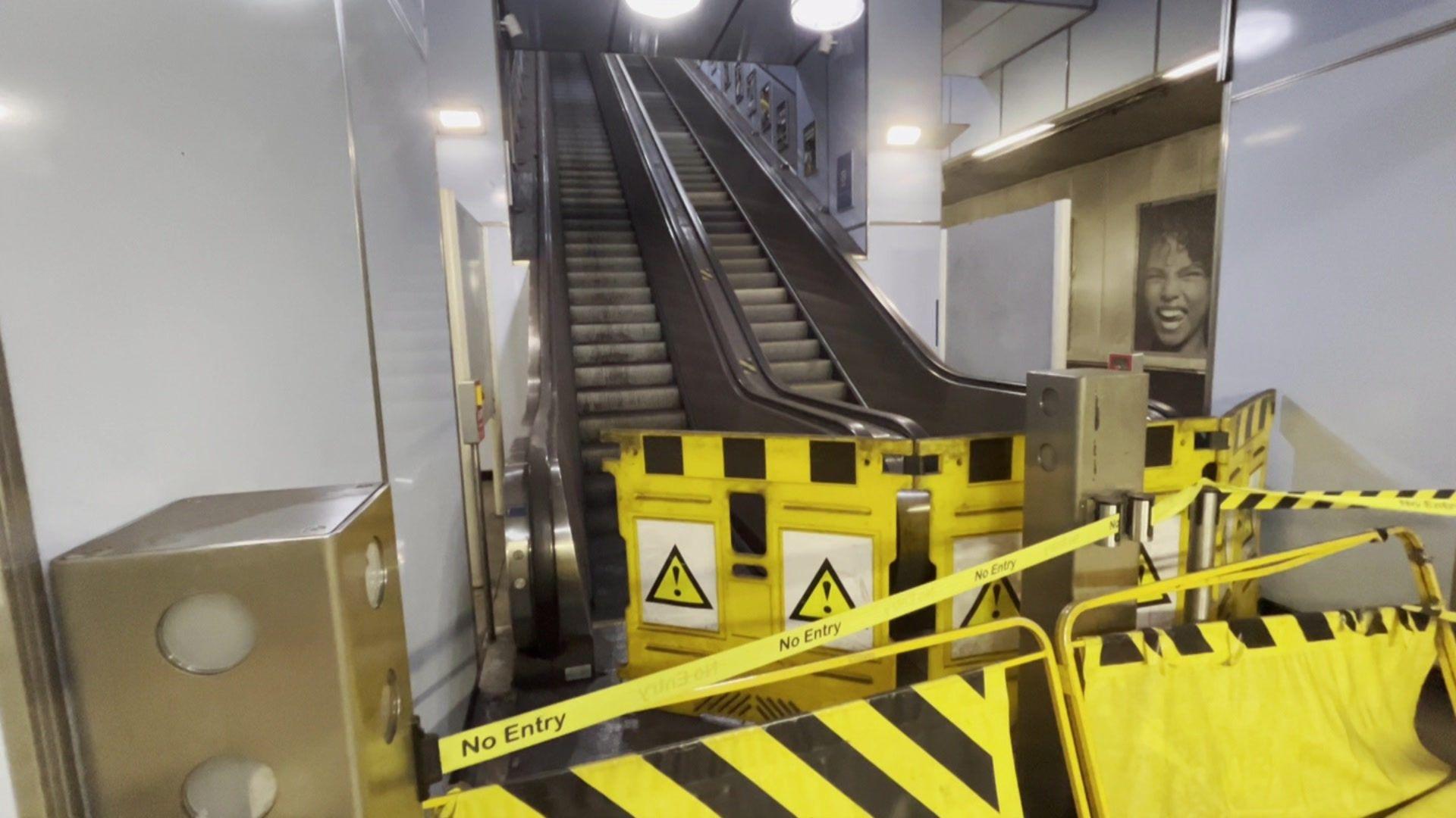 Bottom of two escalators behind yellow 'no entry' tape with yellow warning signs and barriers preventing access