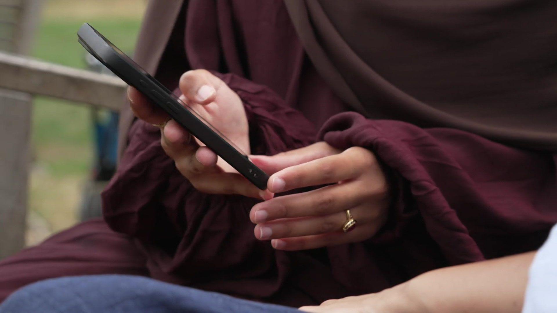 A woman holds a smartphone while sitting on a park bench