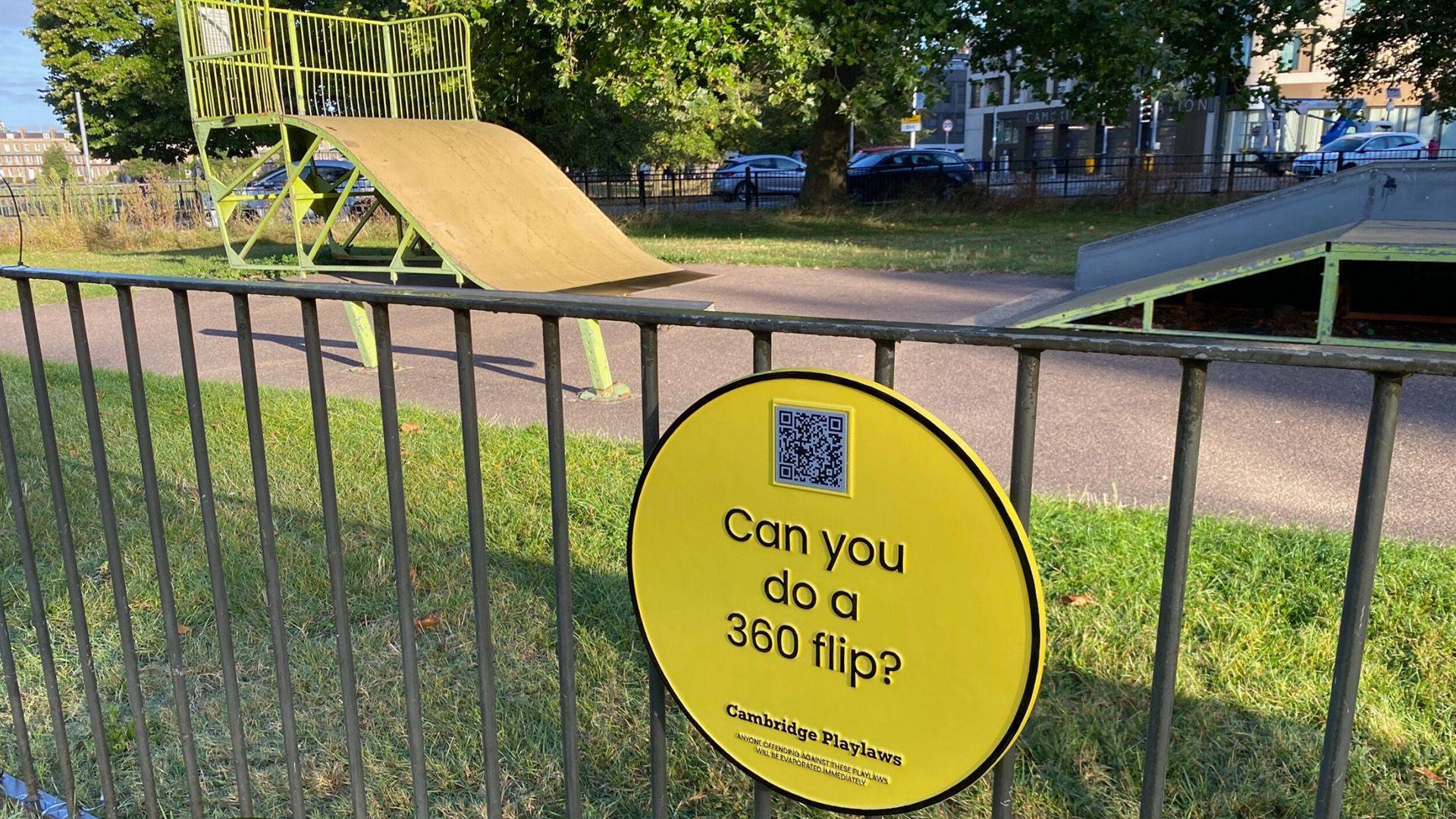 Plaque saying 'can you do a 360 flip?' with the skatepark behind it. 