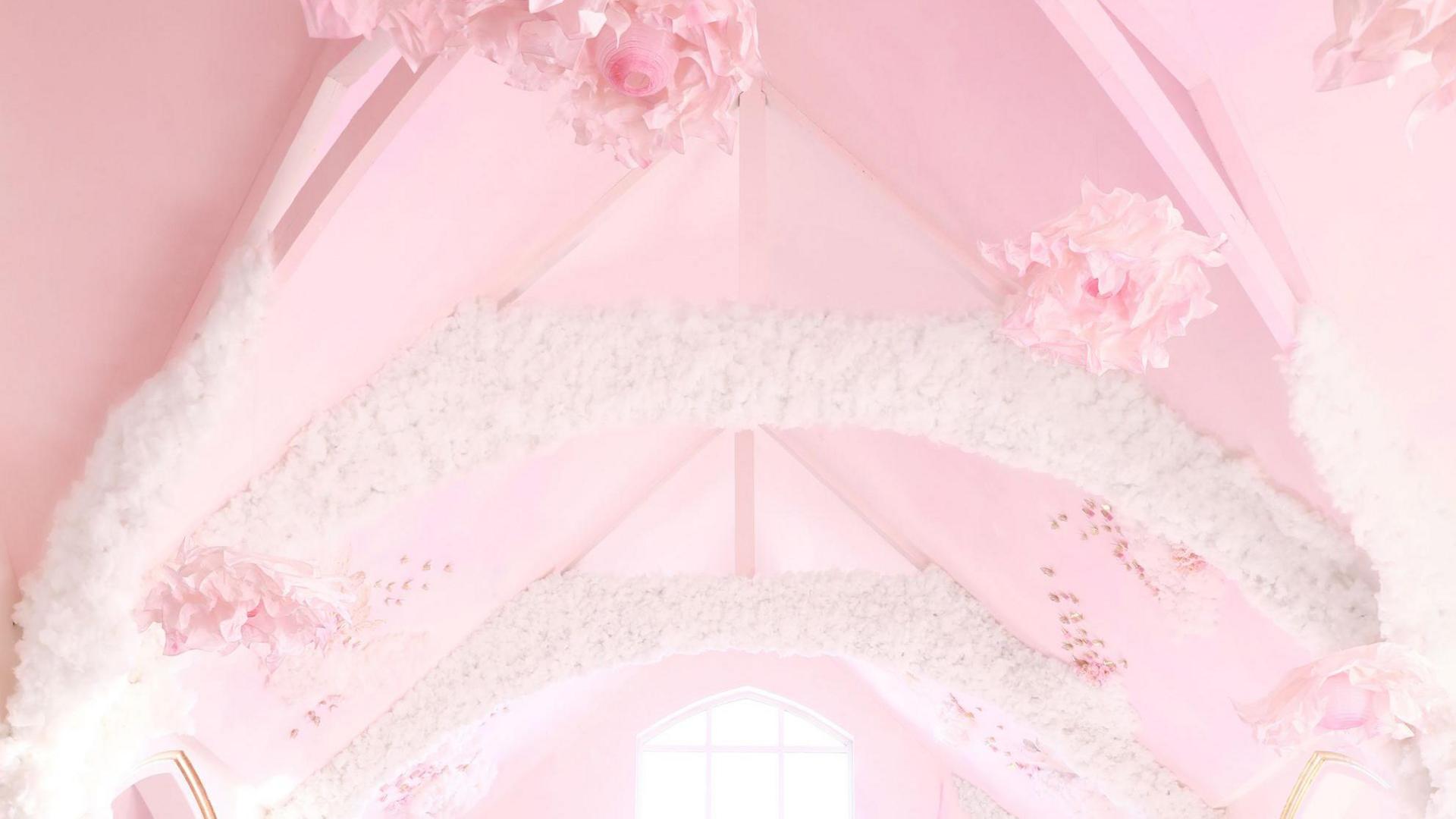 A pink church ceiling with hanging pink flowers and white cloud decoration cascading through