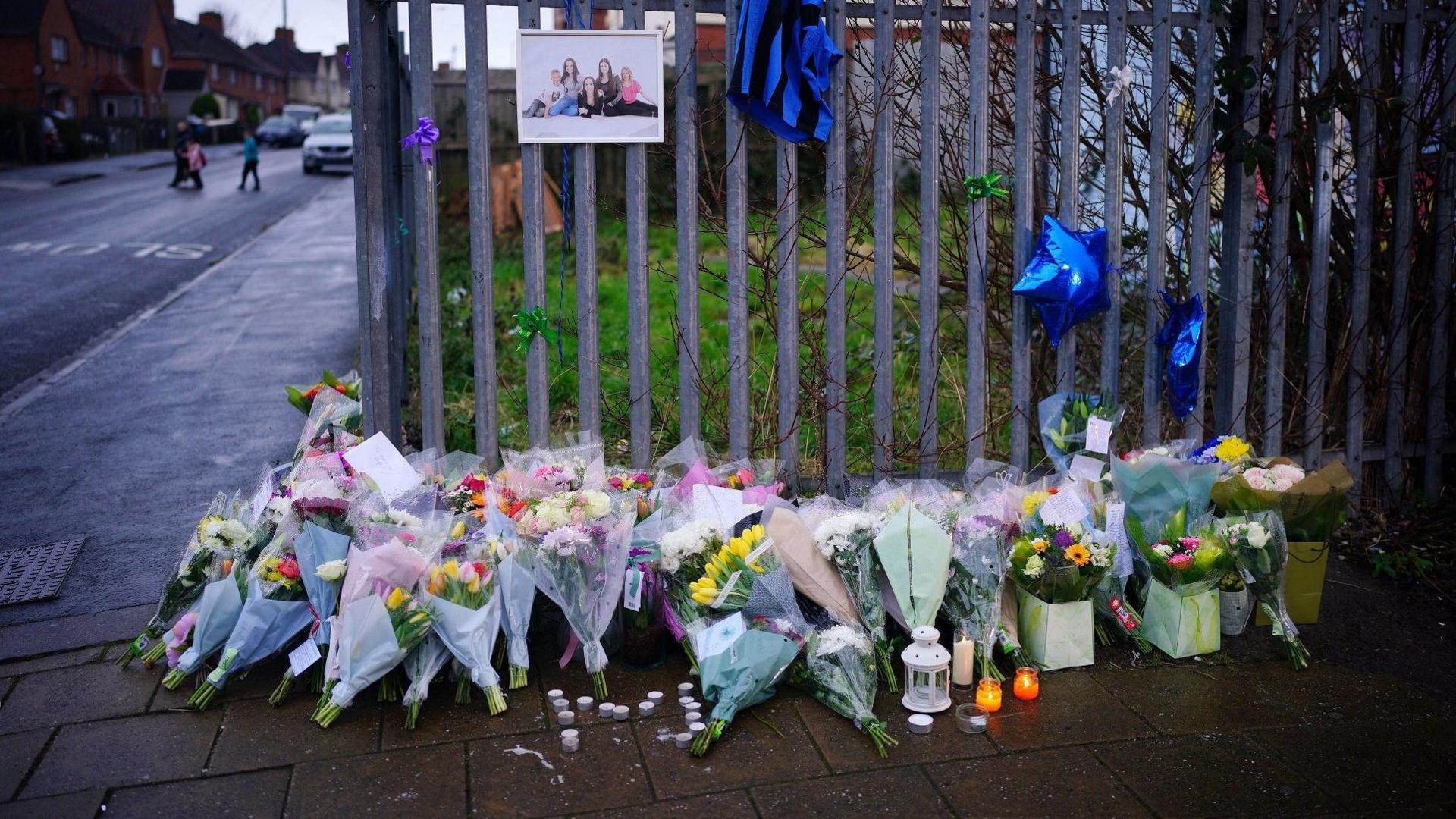 Dozens of floral tributes to Bristol teenagers Mason Rist and Max Dixon are lined up against a blue fence in the Knowle West area of the city