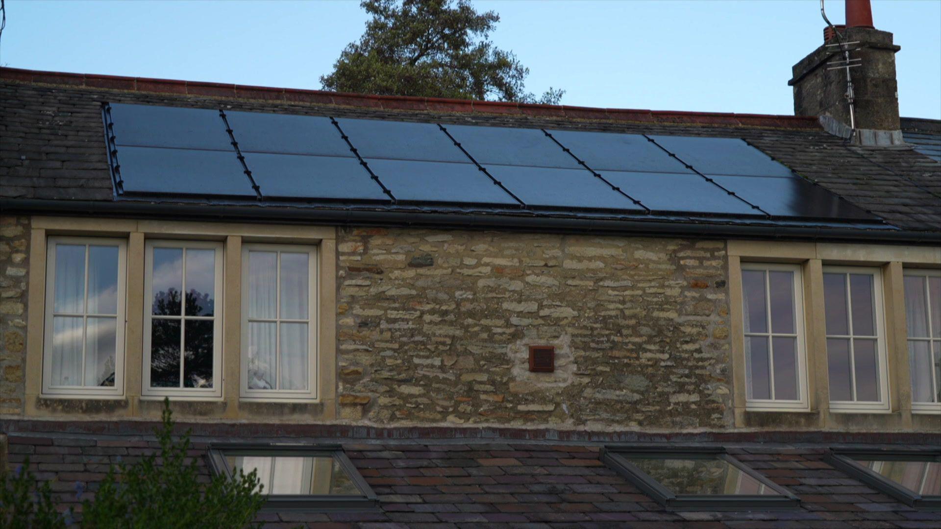 A row of nine black solar panels on the roof of a country cottage style house. 