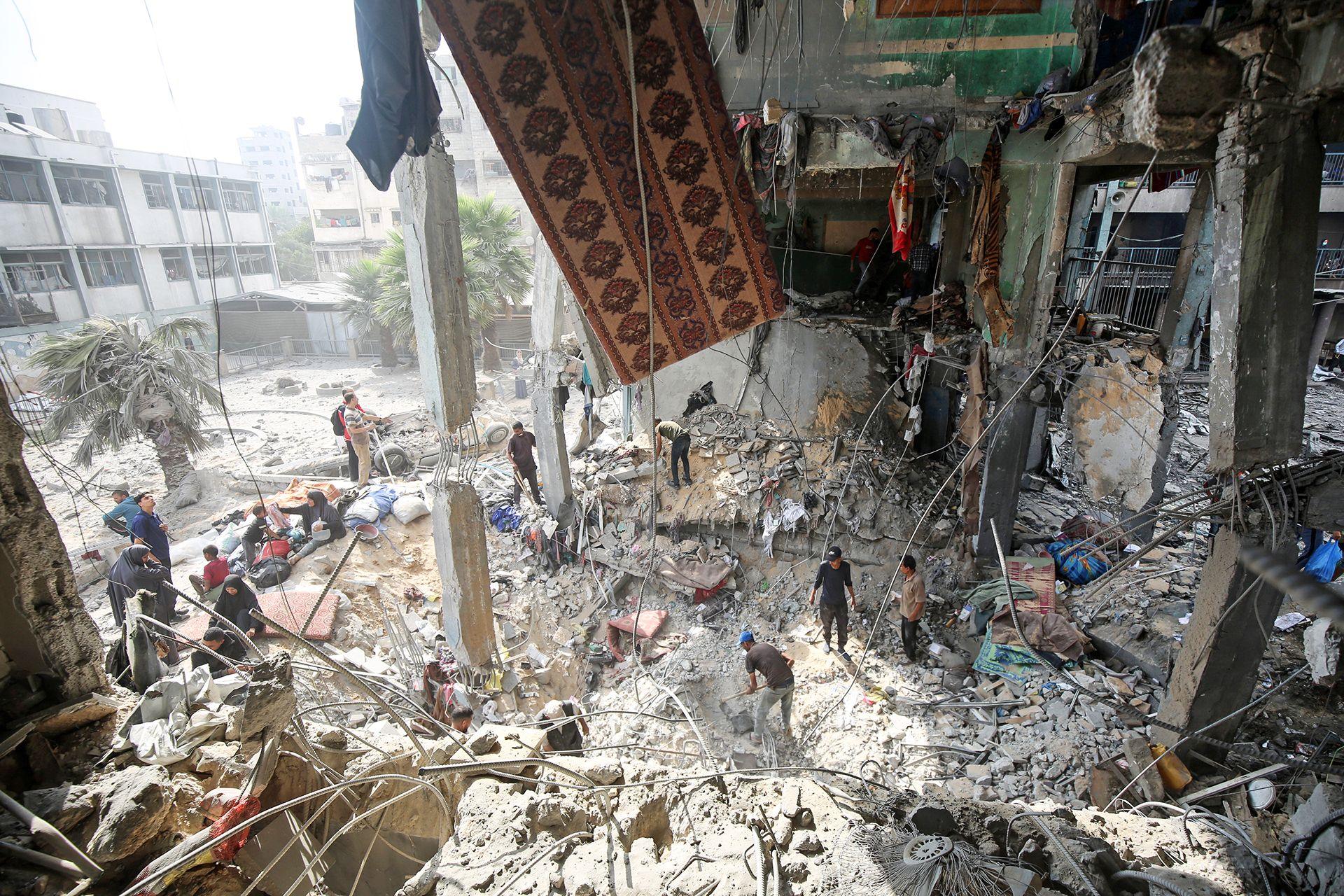 People inspect the damage around a huge crater in a blown-out school caused by Israeli airstrikes, with damage and rubble all around.