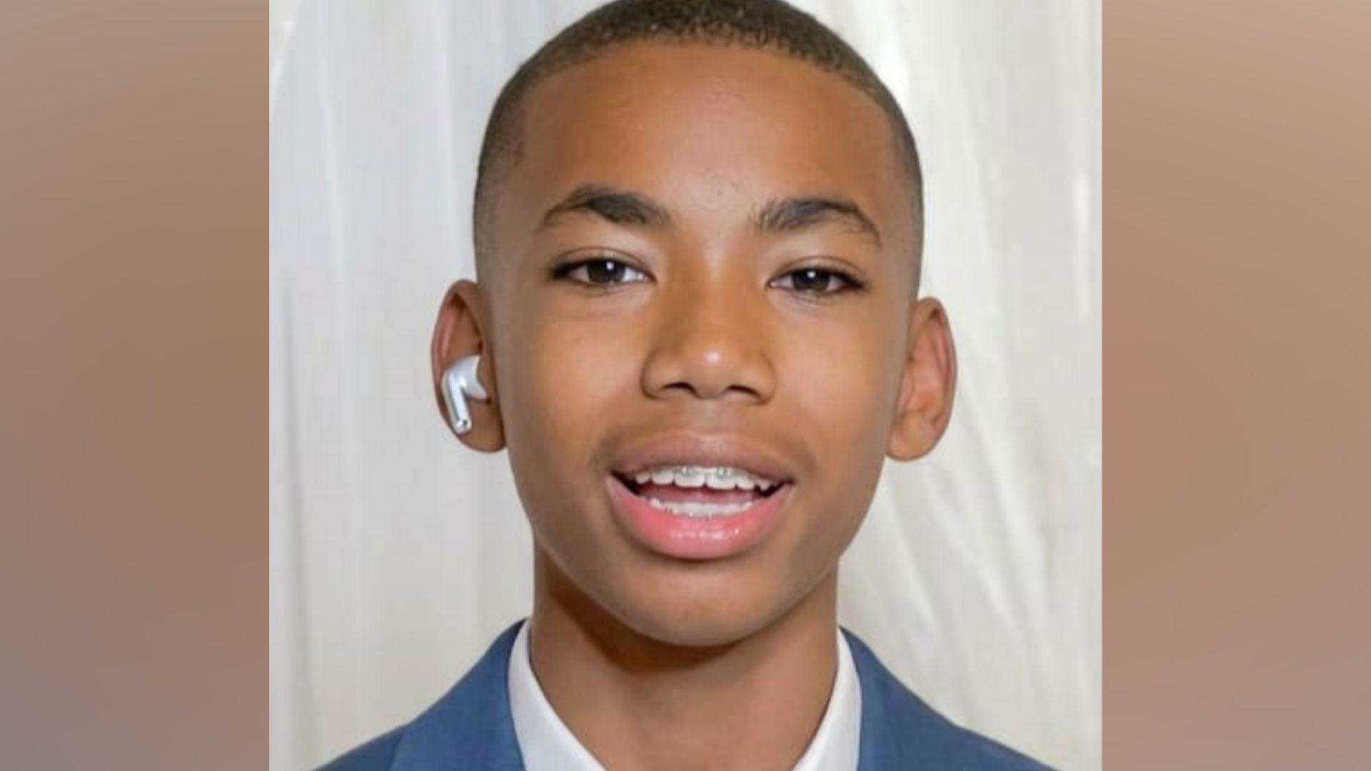 Head shot of Jamal Coombes who is wearing a white shirt beneath a blue jacket. He has a white air pod in one ear