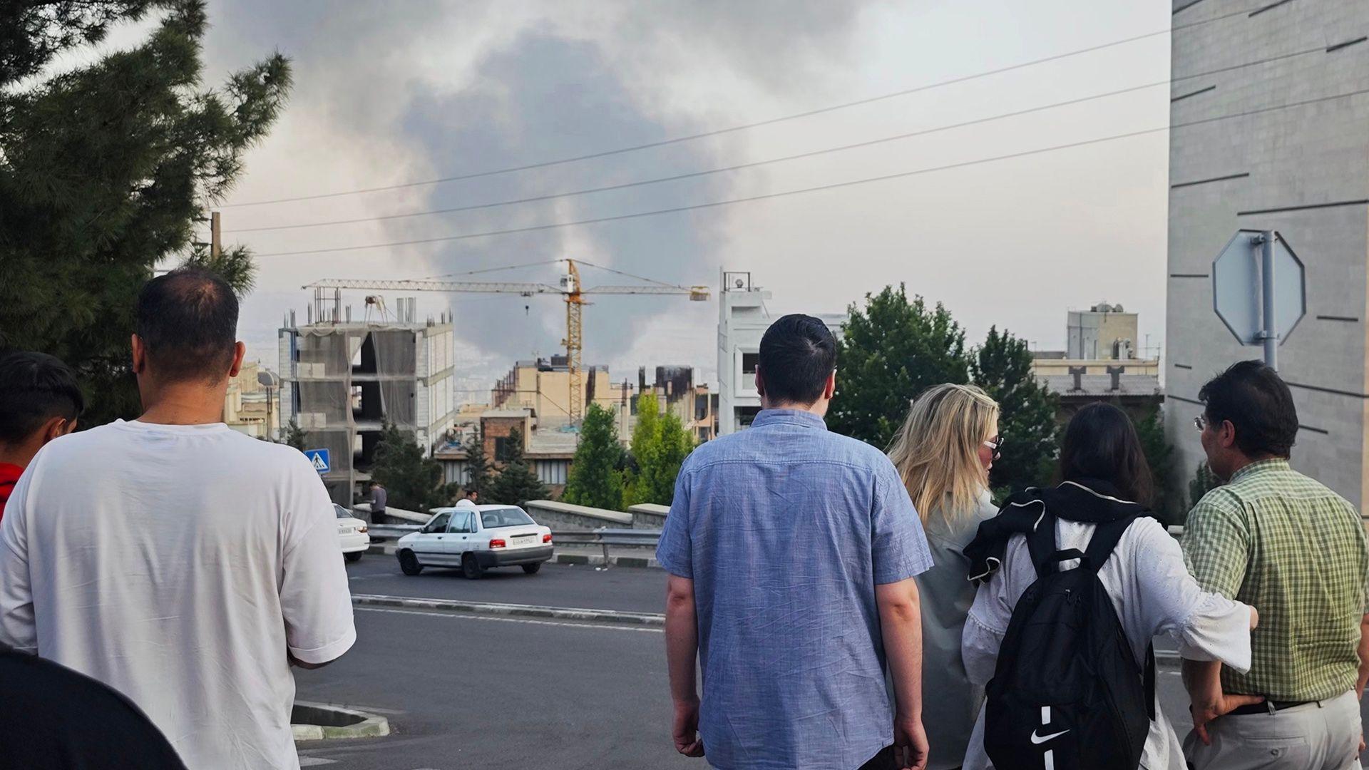 People stand with their backs to the camera as they look at smoke rising in the horizon in Tehran on Monday