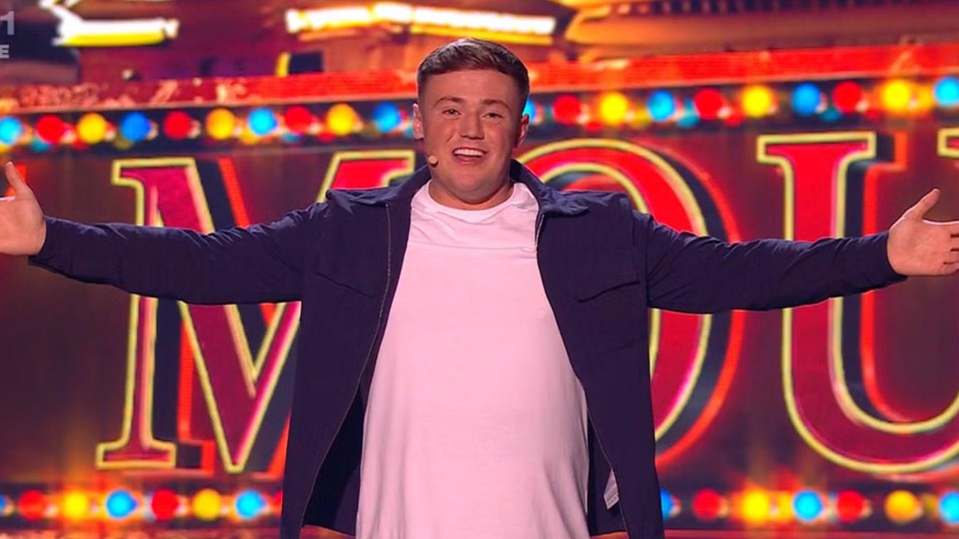 Harry Moulding stands on the stage looking down the camera with his arms outstretched