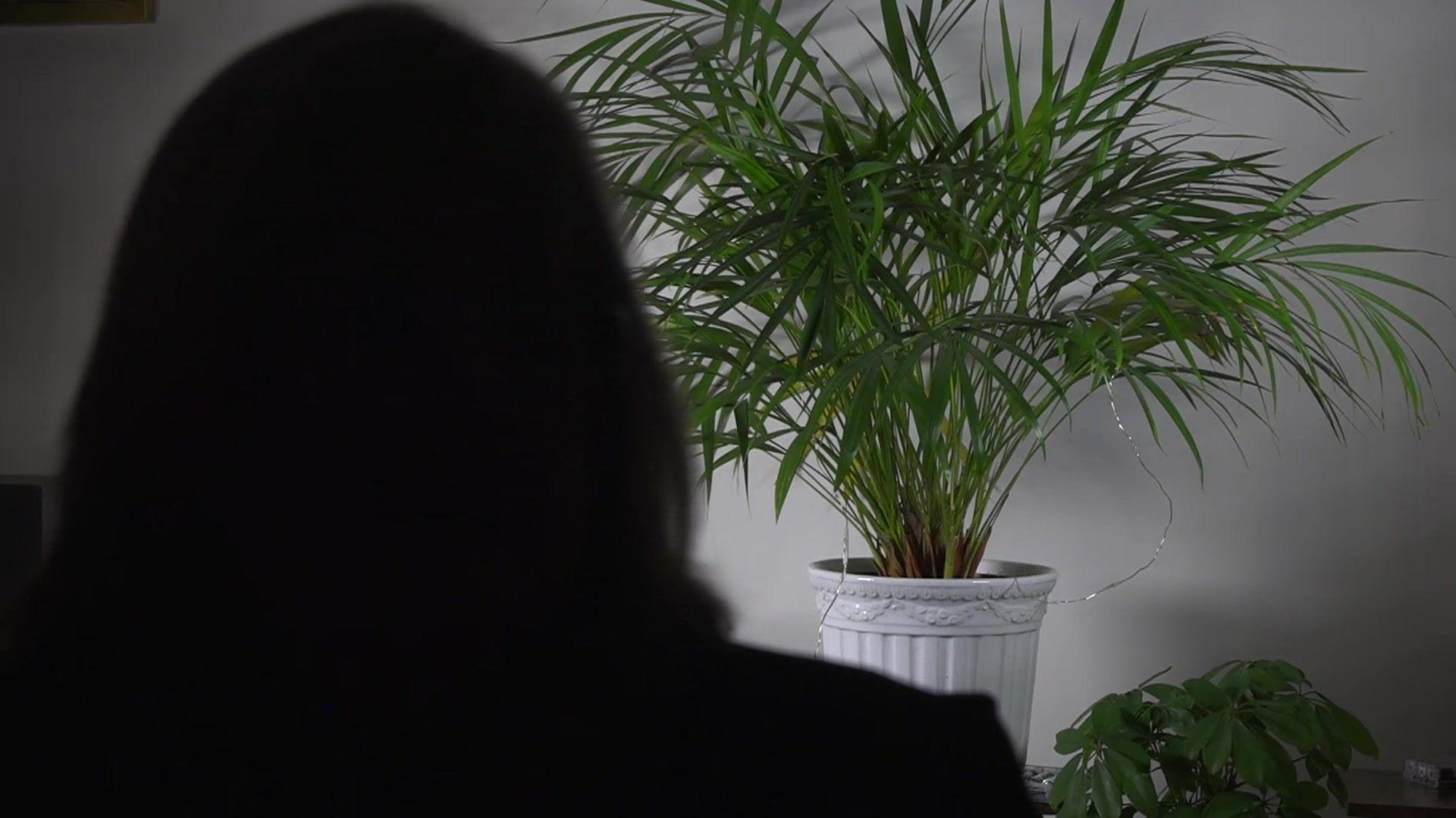 A silhouette of a woman in a darkened room with a pot plant in the background. 