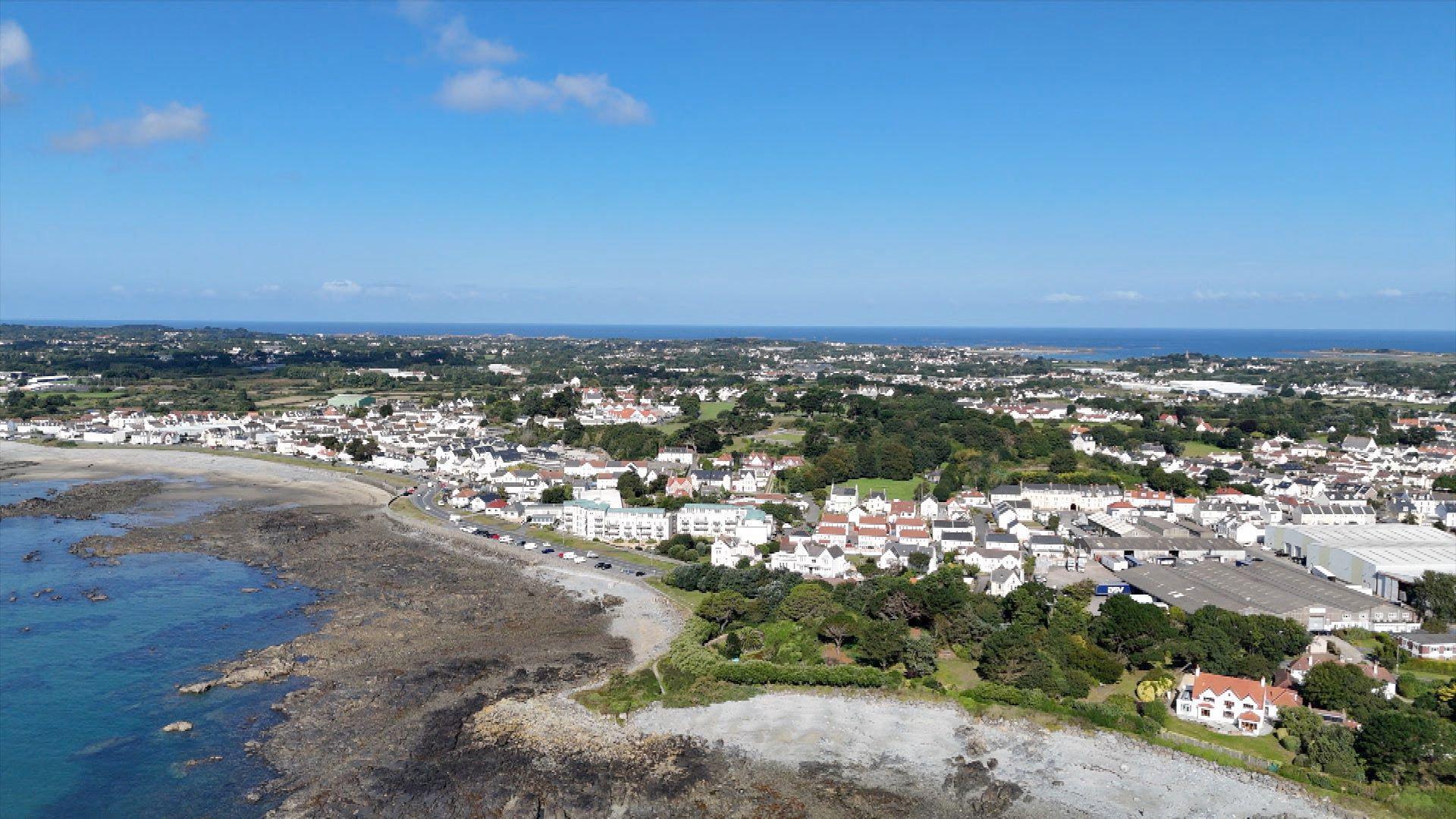 A drone shot of a part of Guernsey. You can see the grassland with houses and water.