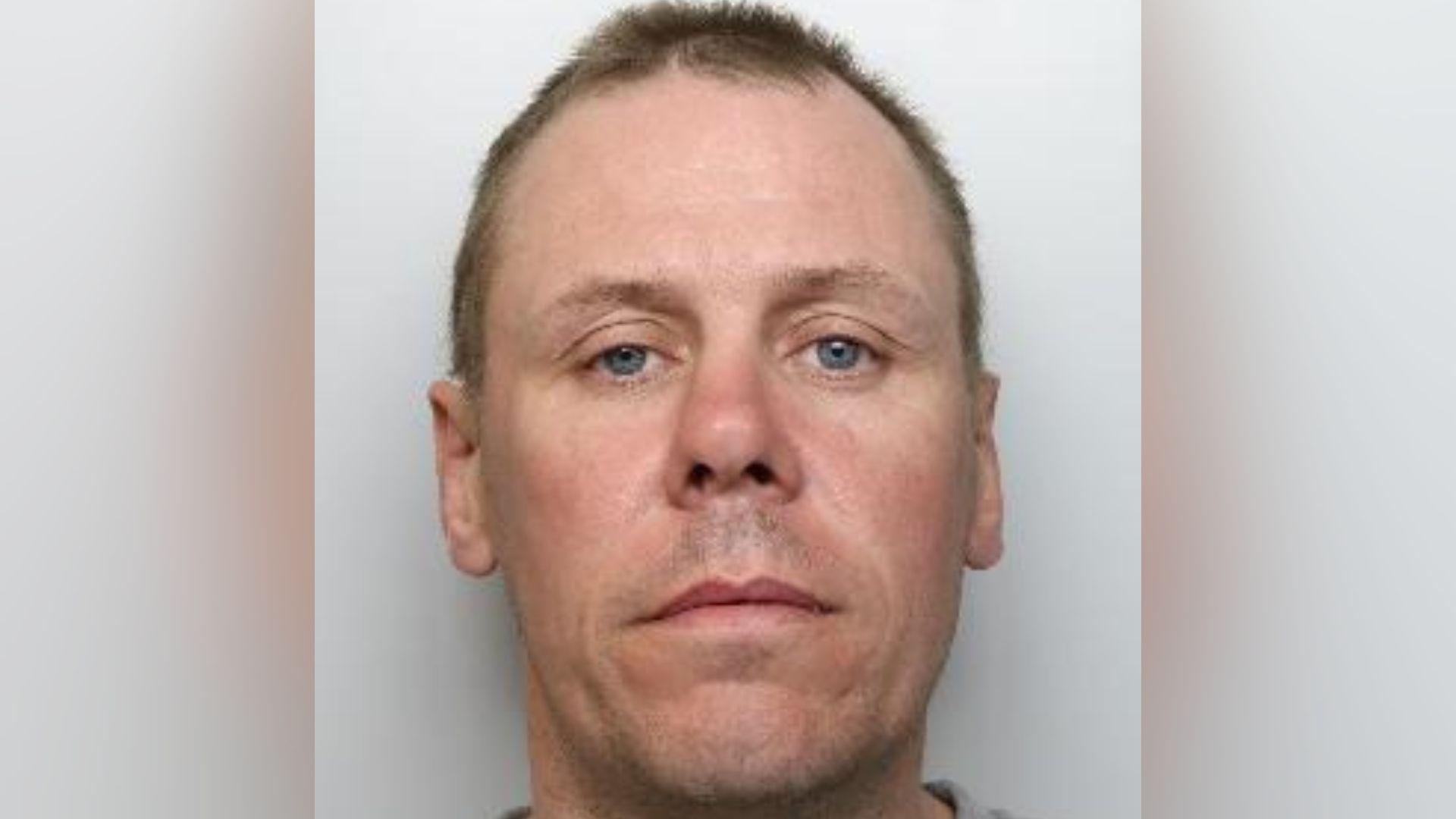 Mugshot of a man with short brown hair and an oval face. He has blue eyes and a slightly crooked nose. He has a neutral expression.