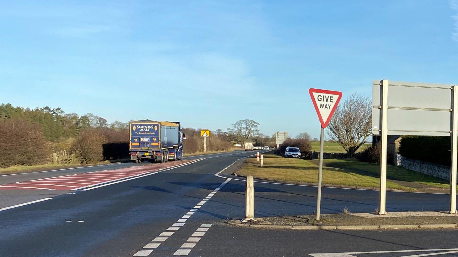 A single carriageway stretch of the A1 in Northumberland taken from a junction with a lorry going past. There are a number of cars further along the road.