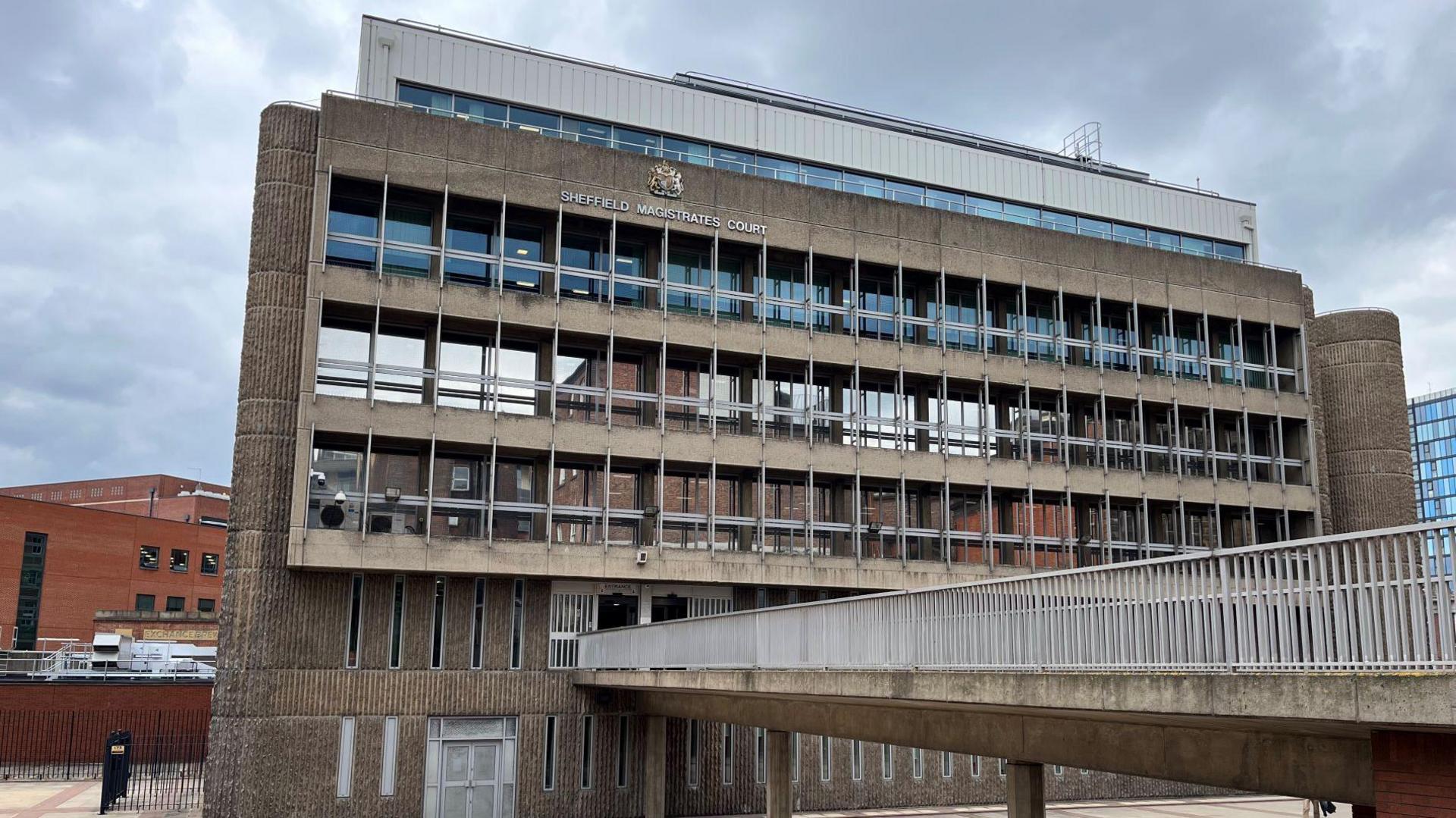 A footbridge leads to the building which stretches over several floors and has glass windows along the front. 