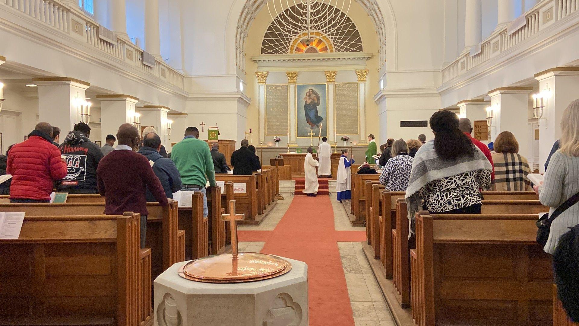 Pictured here is the church in the modern day. This colourful photograph from the back of the church is facing the alter with a copy of Raphael's Sistine Madonna at its centre. The congregation is stood, facing the alter, engaged in worship as clergymen lead at the front. 