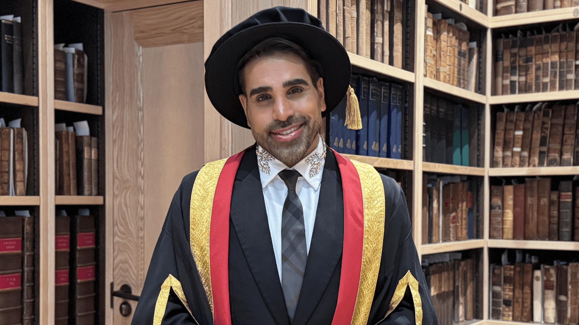 Dr Ranj Singh in a black cap and gown with gold and red trimmings.