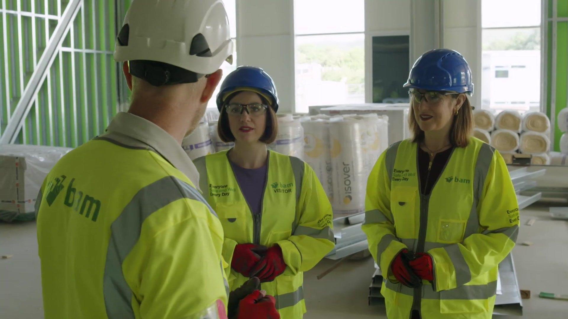 Bridget Phillipson and Rachel Reeves wear hi-vis and PPE while talking to a building worker.