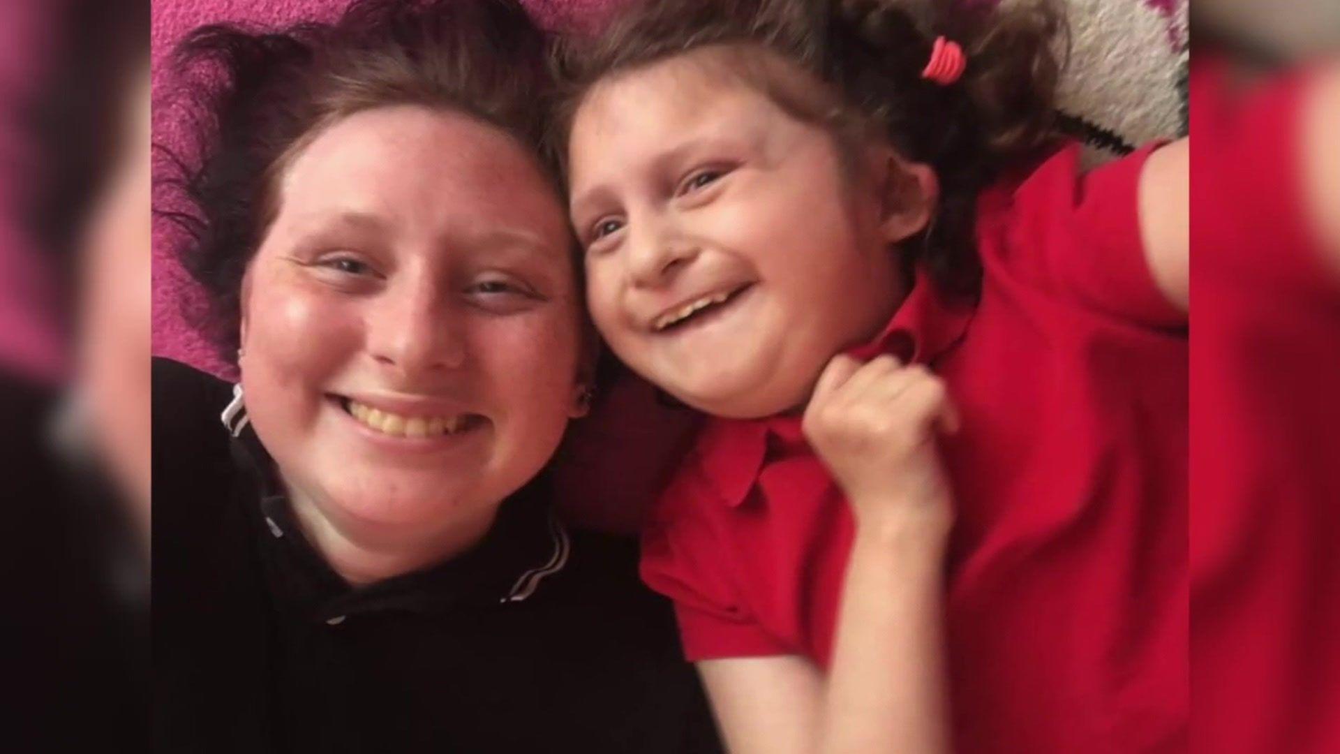 A girl and her younger sister smiling while taking a selfie. They appear to be laying down on a bed.