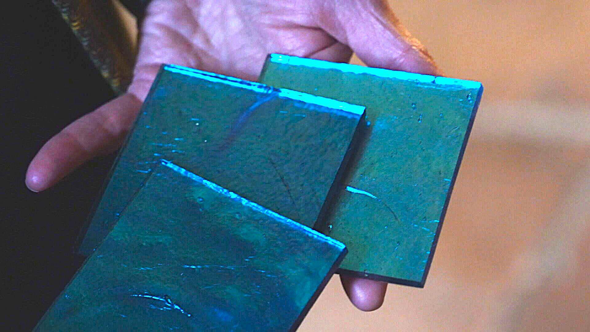 A hand holds three glass tiles in shades of shimmering blues.