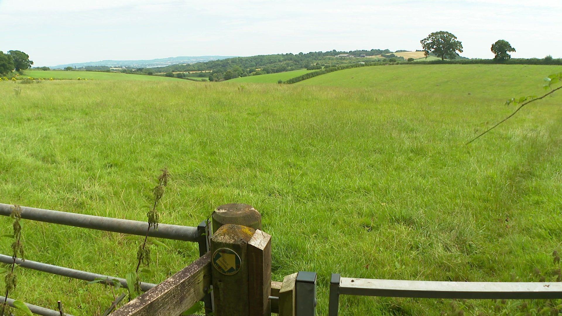 A gate with a countryside path sign in the foreground and looking out over fields near Kennford.