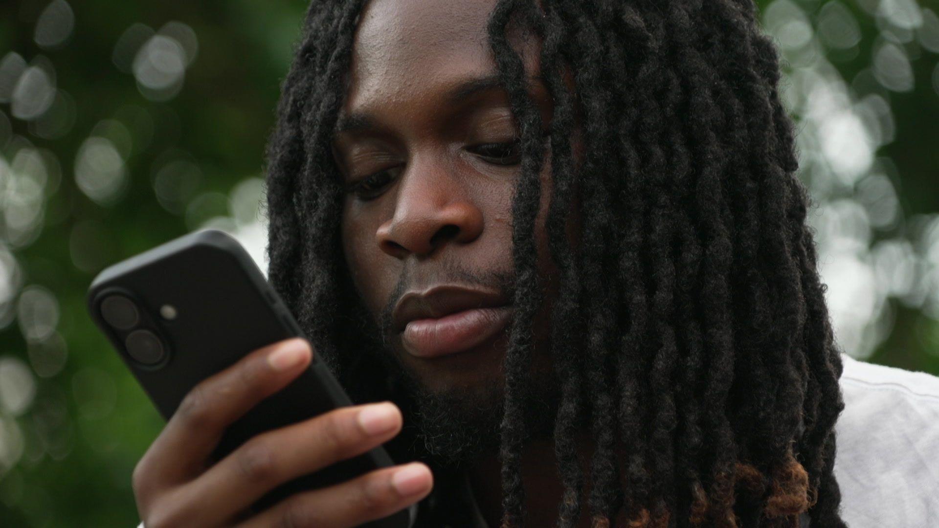 Prince is sitting in a garden on a sunny day and looking at his mobile phone