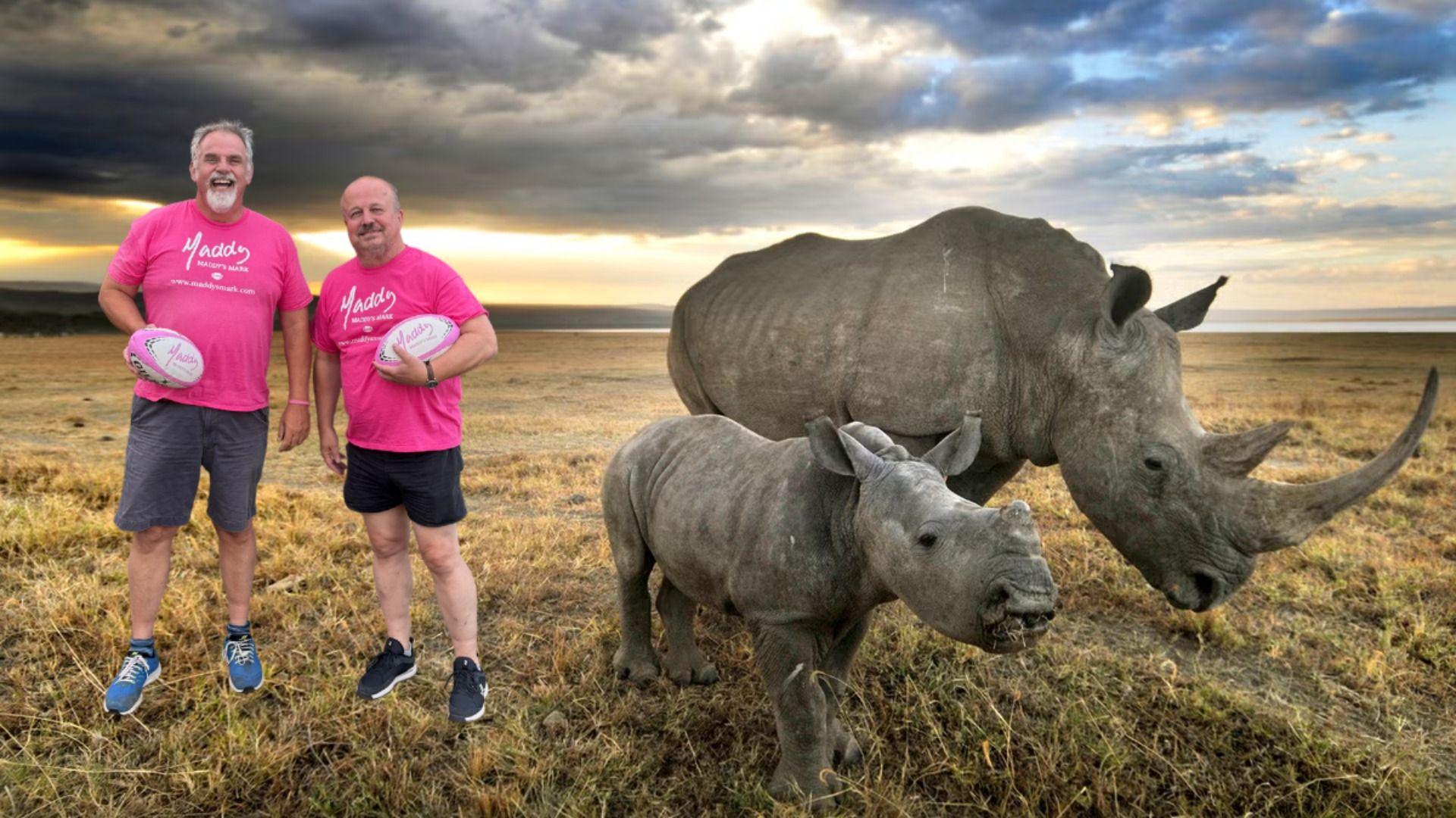 Simon Lawrence and David Cosway both wear pink t-shirts and are holding rugby balls. The image seems to have been edited to look as though they are stood next to two rhinos.