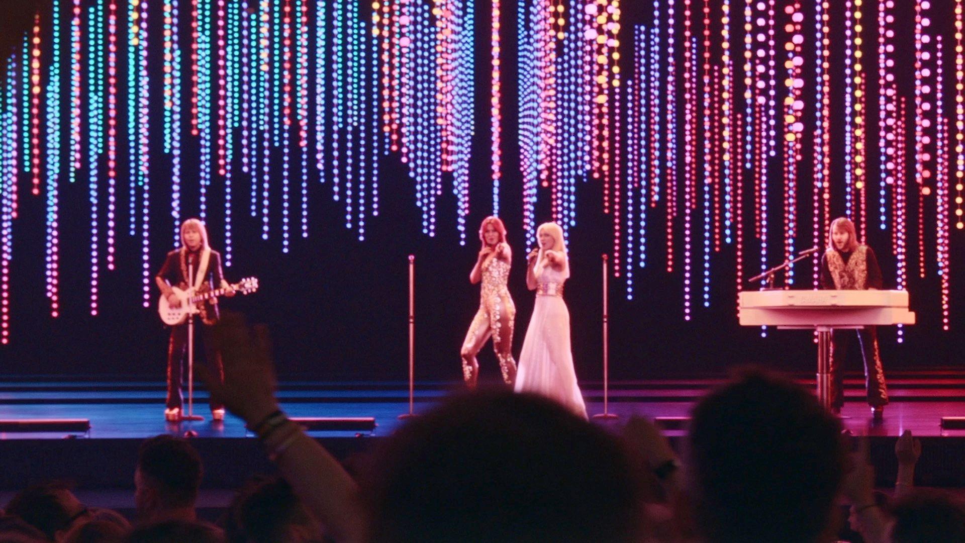 The Abba Voyage avatars on stage. Bjorn plays guitar, Benny a piano, with the singers centre stage, both pointing to the crowd. The 3D figures look very realistic.