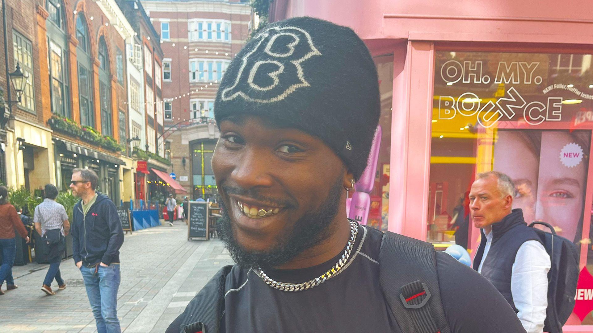 A man wearing a black beanie smiling at the camera on a street