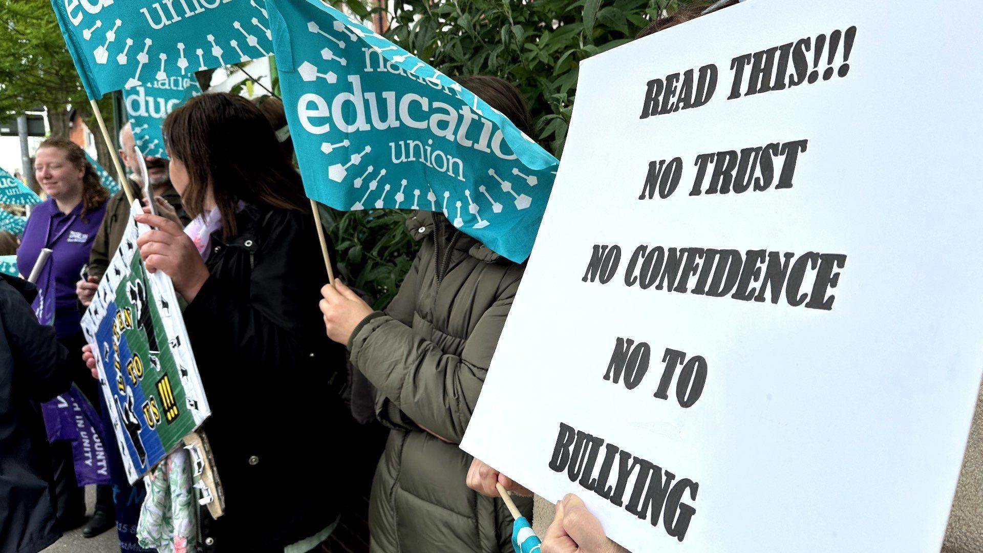 Protesters holding banners and waving flags. One banner reads: "No trust, no confidence, no to bullying"